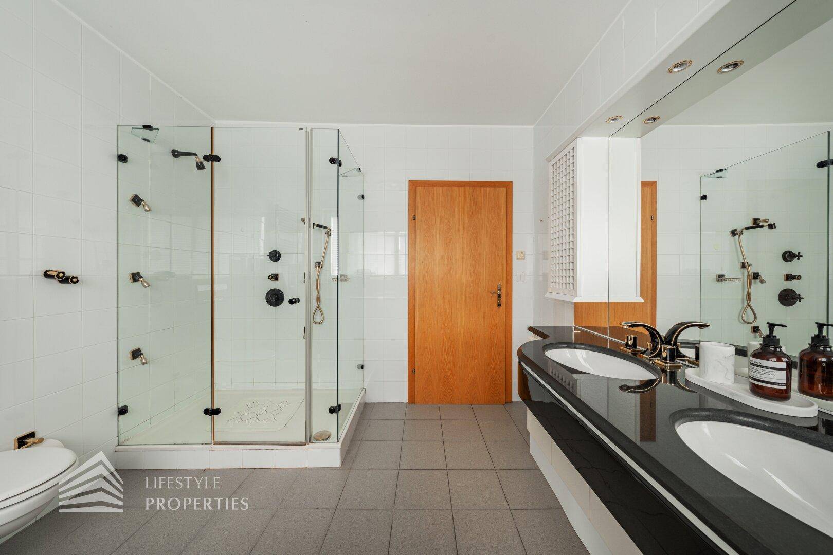 Geräumiges Badezimmer mit Doppelwaschbecken, großer Dusche und Fliesenboden.