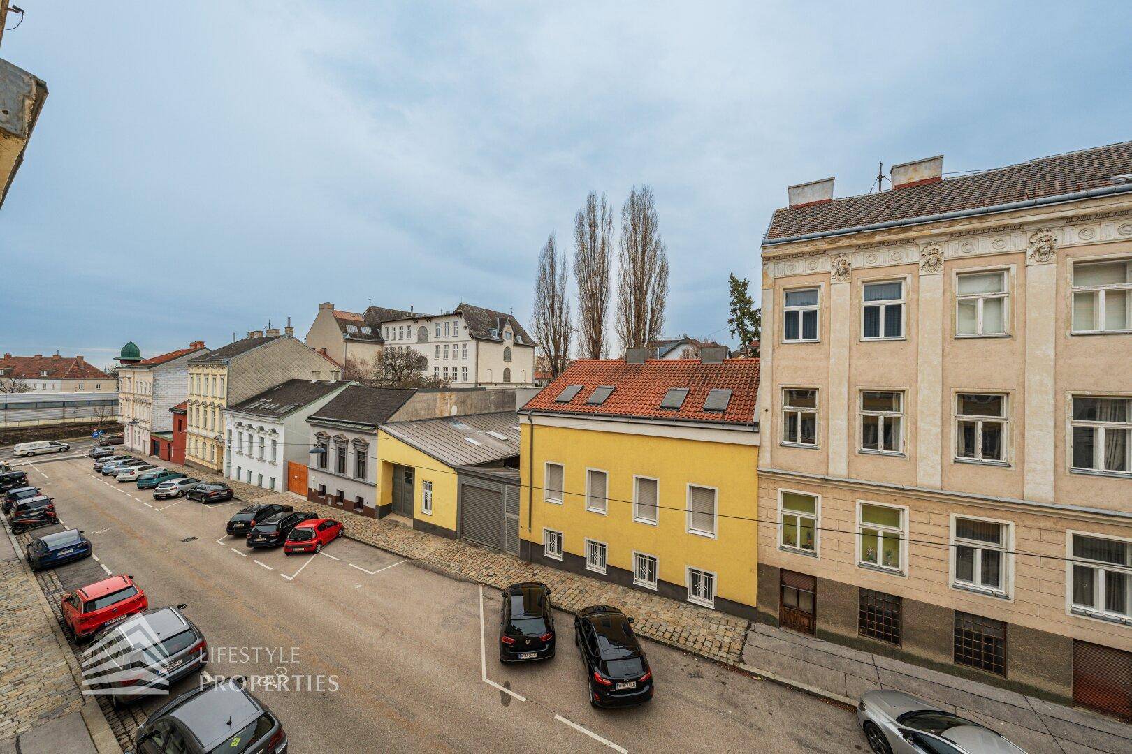 Blick von oben auf eine ruhige Straße mit parkenden Autos und umliegenden Gebäuden.