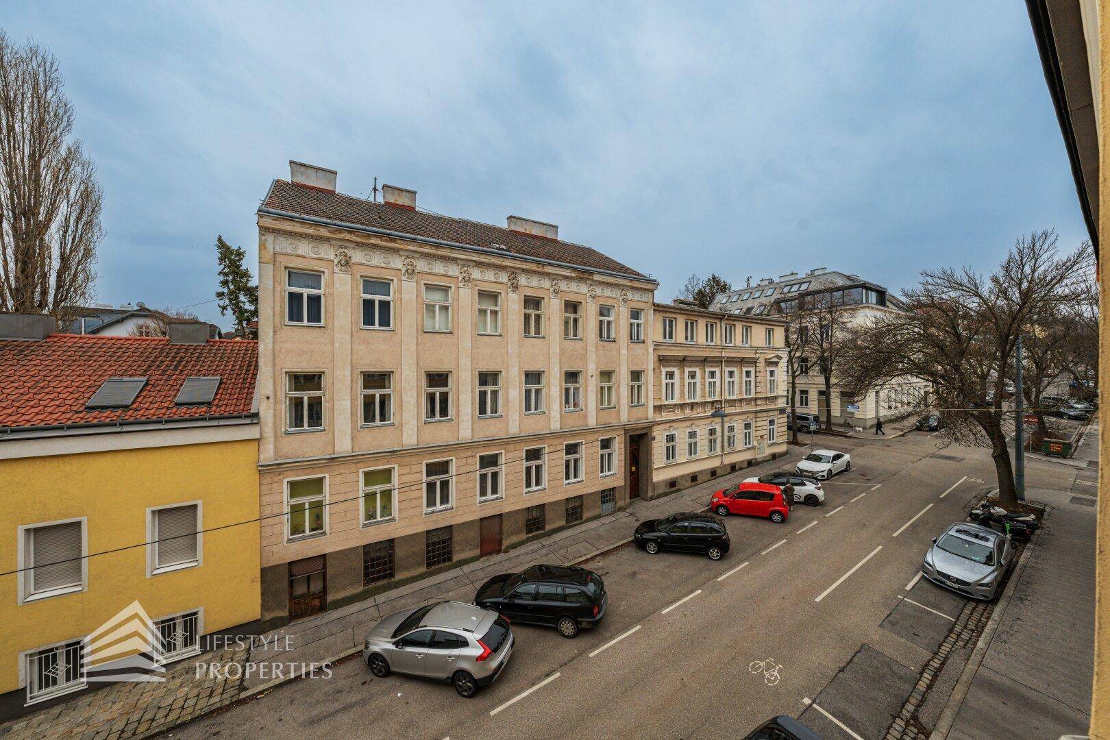 Panoramablick auf eine Wohnstraße mit historischen Gebäuden und parkenden Fahrzeugen.