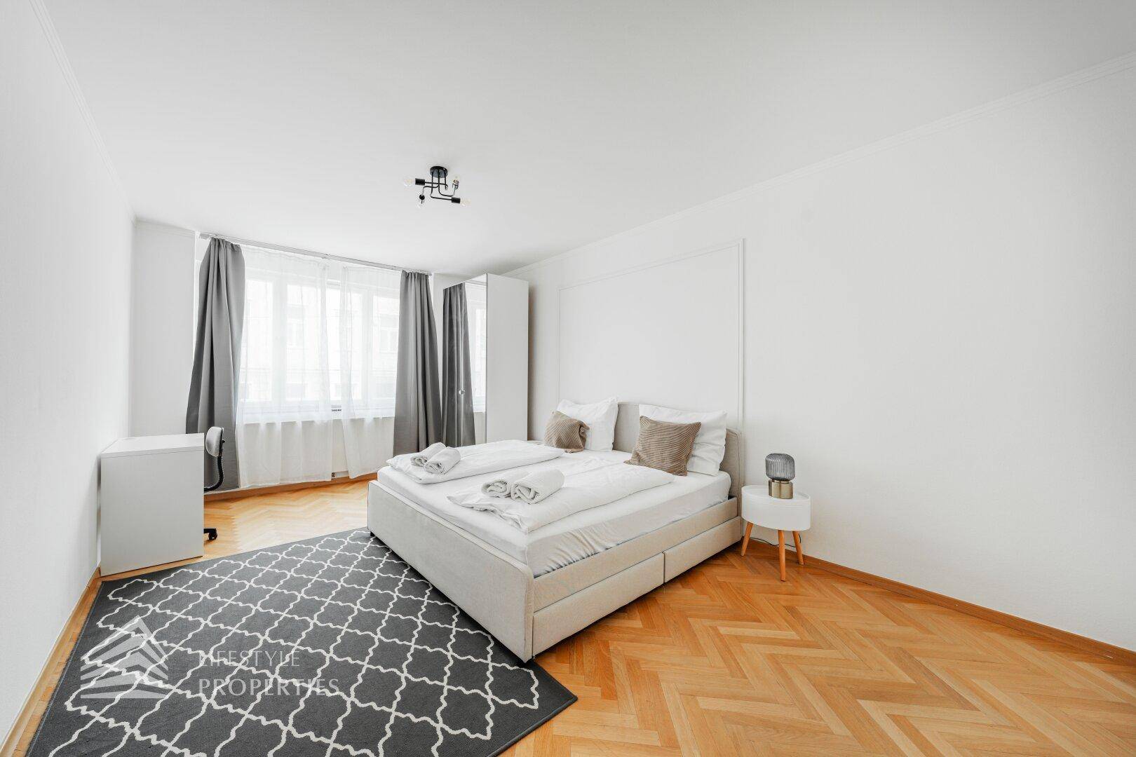 Helles Schlafzimmer mit Parkettboden, Doppelbett und großem Fenster.