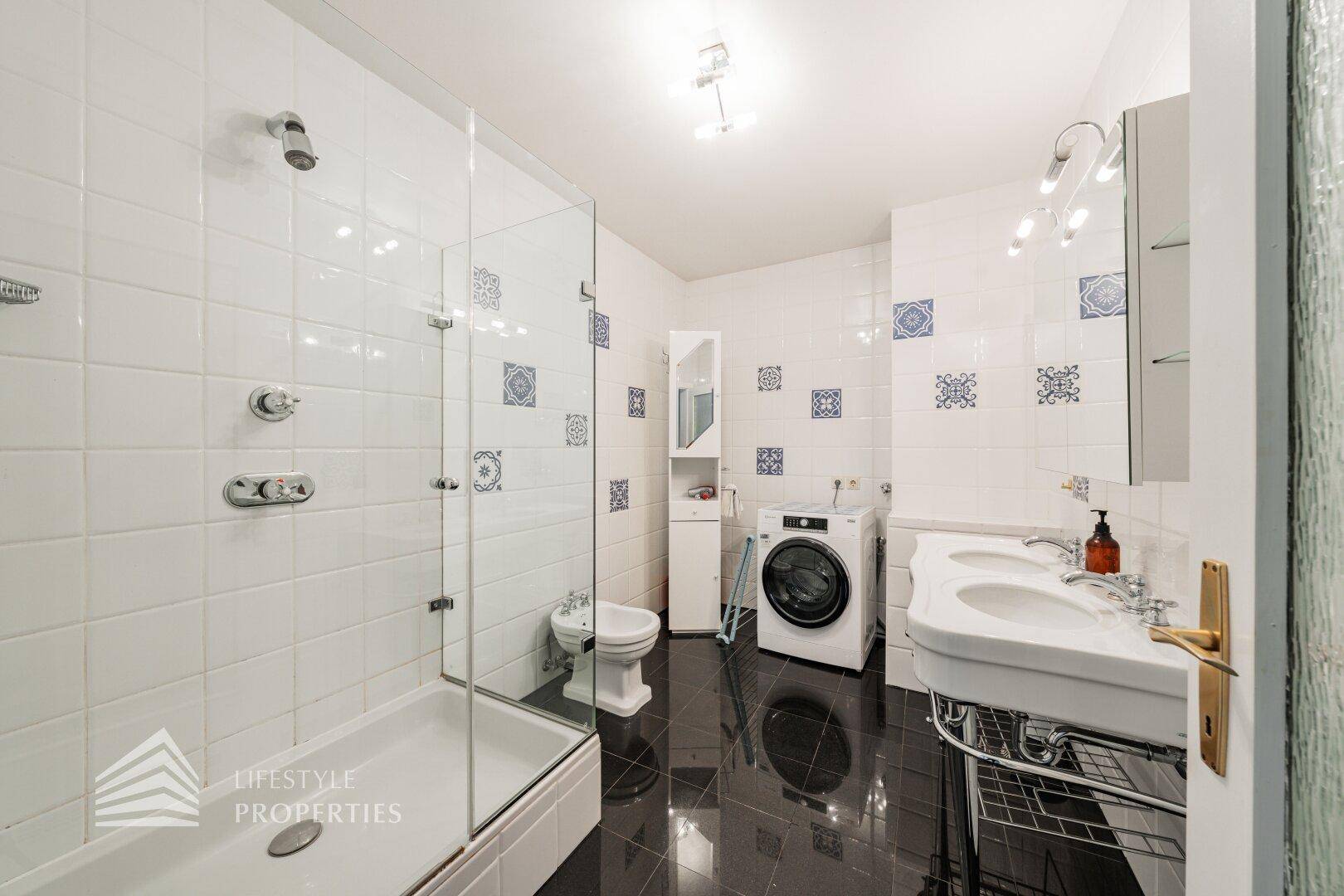 Helles Badezimmer mit Dusche, Doppelwaschbecken und Waschmaschine.