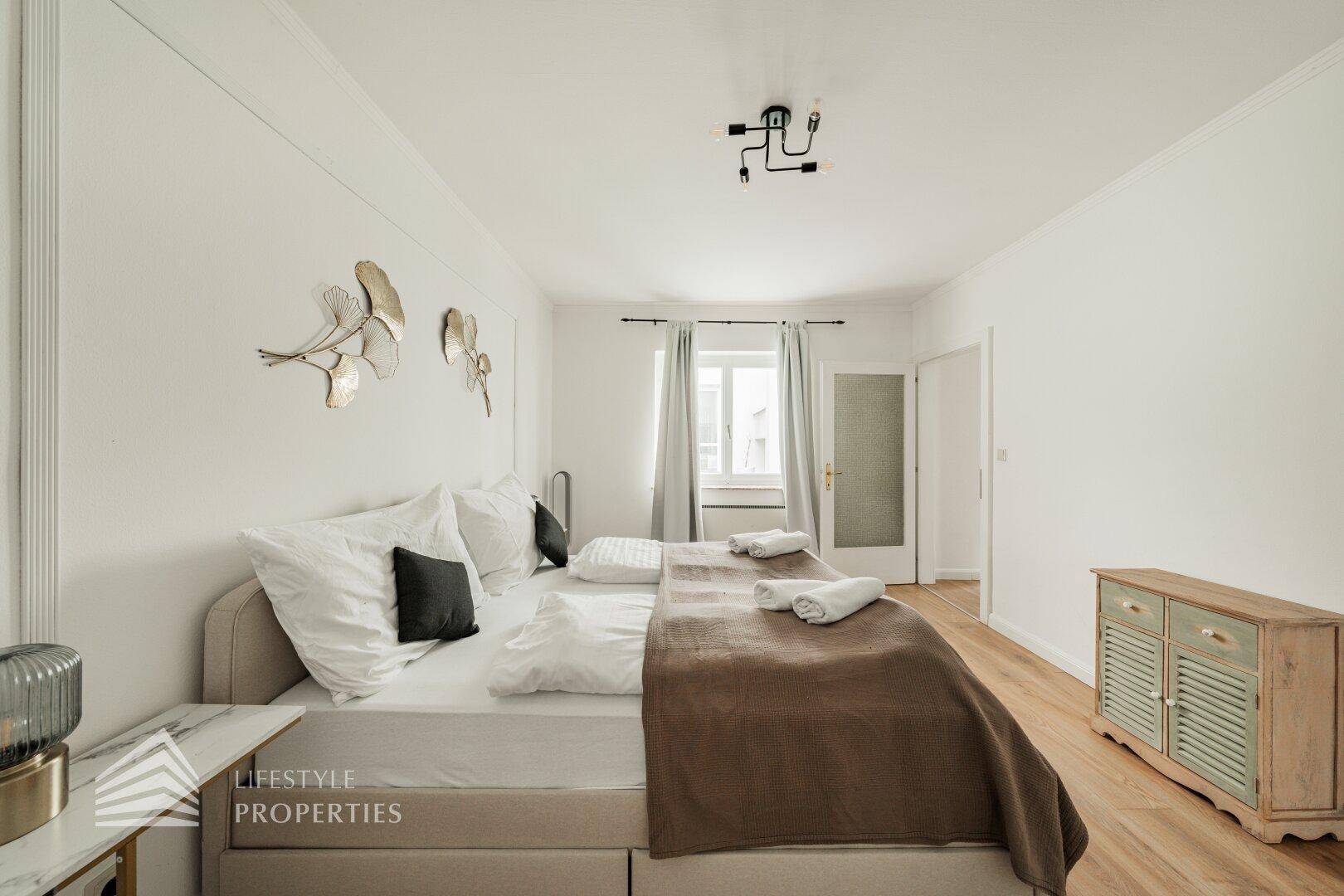 Schlafzimmer mit Holzboden, Doppelbett und dekorativer Wandgestaltung.