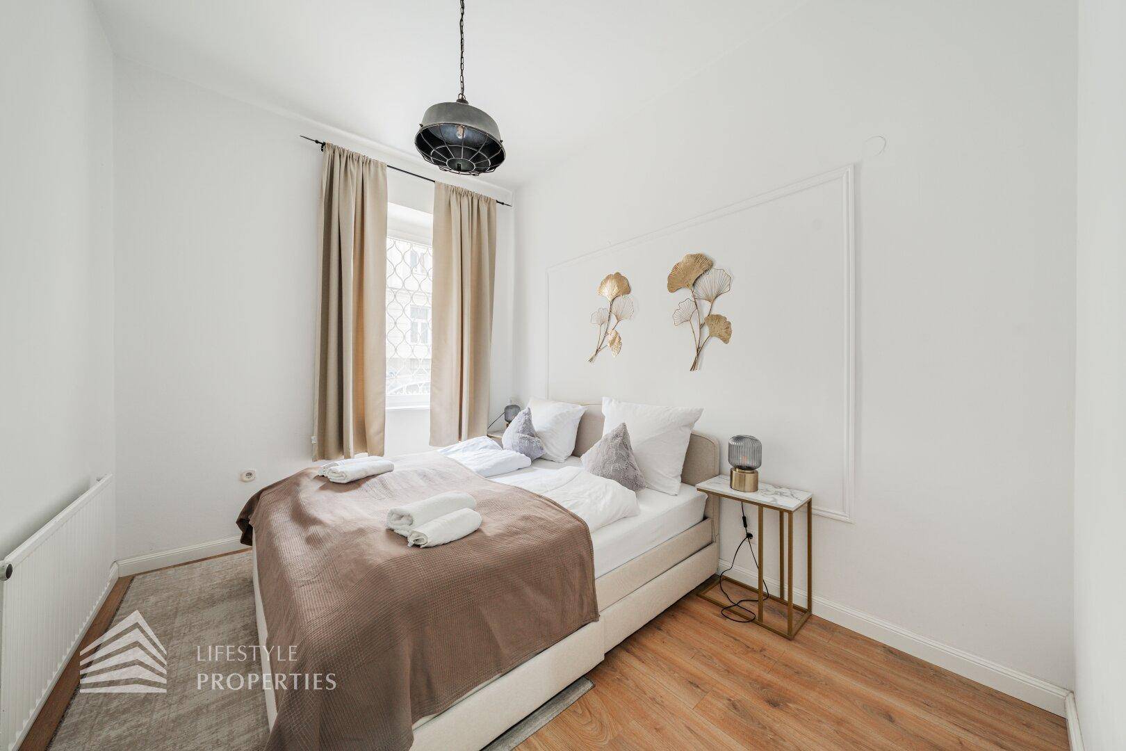Helles Schlafzimmer mit Holzboden, Doppelbett und modernem Beistelltisch.