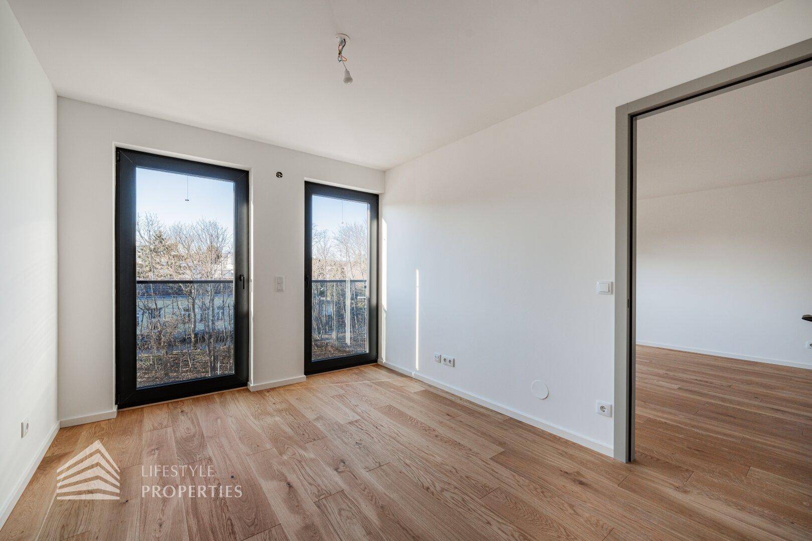 Heller Wohnraum mit schönem Parkettboden und zwei hohen Fenstertüren, die viel Licht hereinlassen.