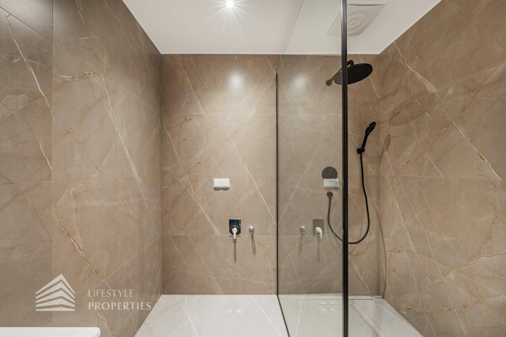 Detailansicht der modernen begehbaren Dusche mit eleganten Fliesen und schwarzen Armaturen.