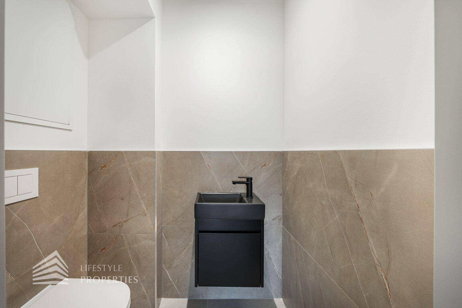 Modernes Gäste-WC mit stilvollem schwarzen Waschbecken und Wandfliesen.