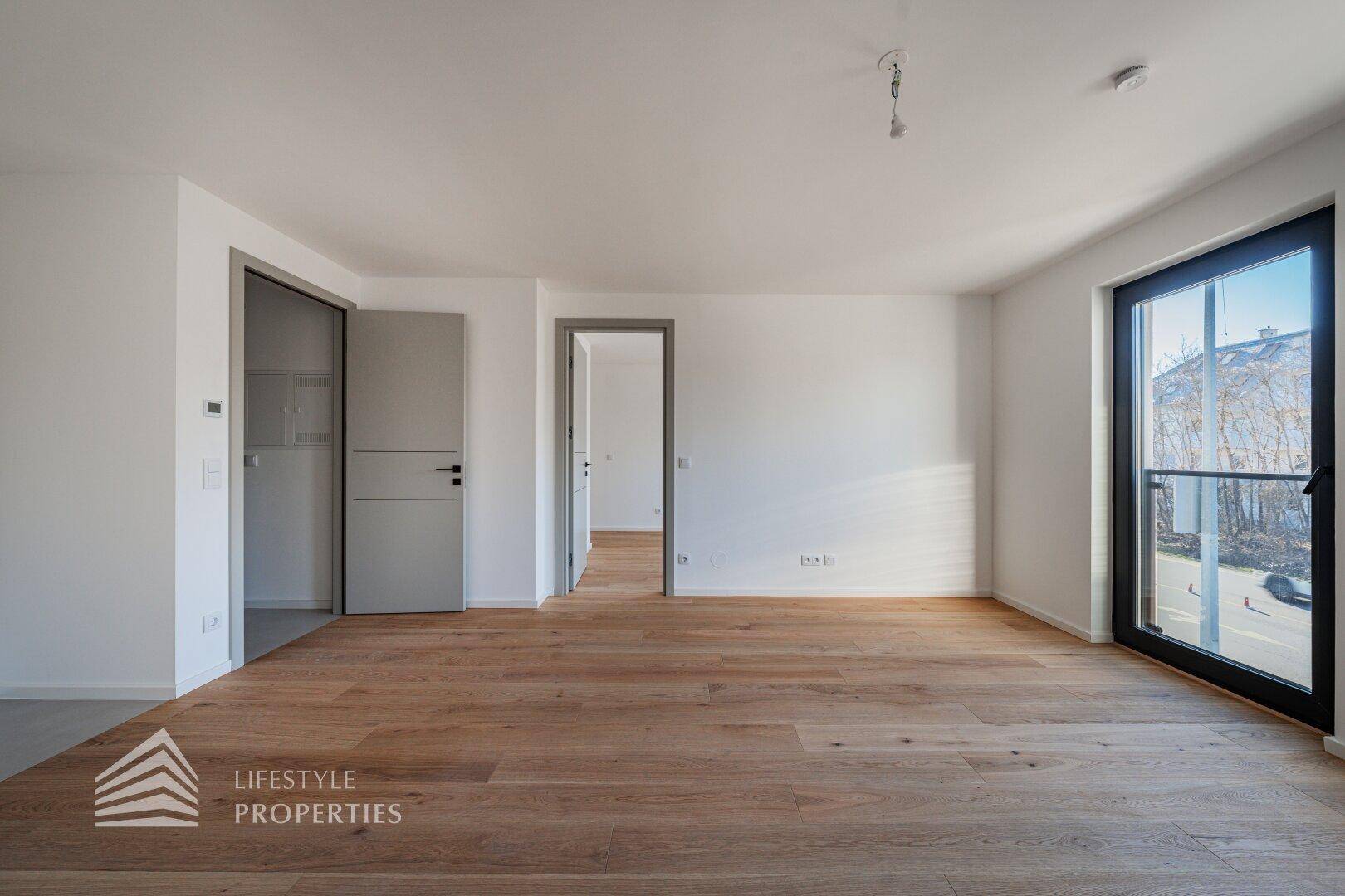 Lichtdurchflutetes Zimmer mit Holzboden und einer Fenstertür, die nach draußen führt.