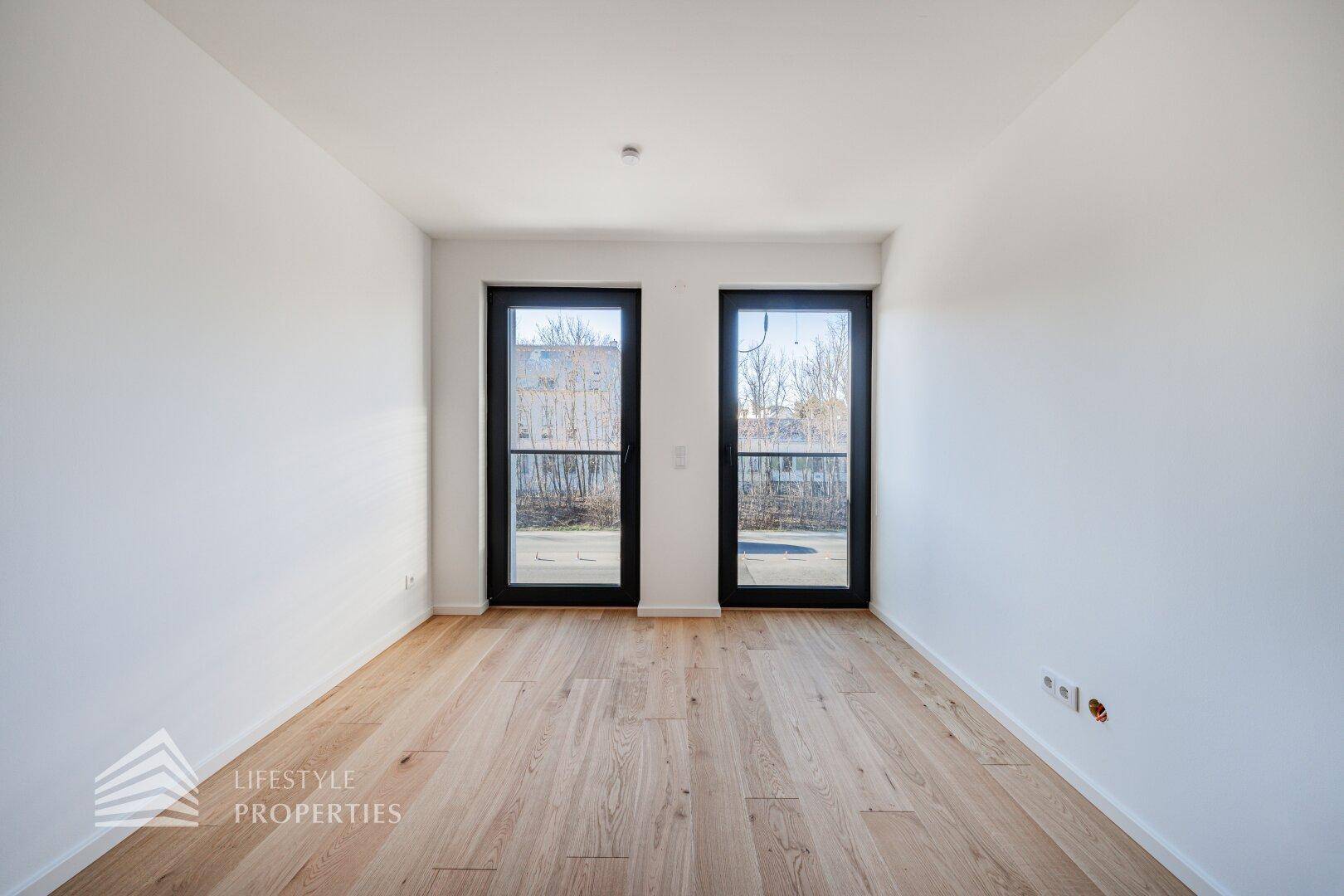 Helles Schlafzimmer mit Holzboden und zwei Fenstertüren für viel Tageslicht.