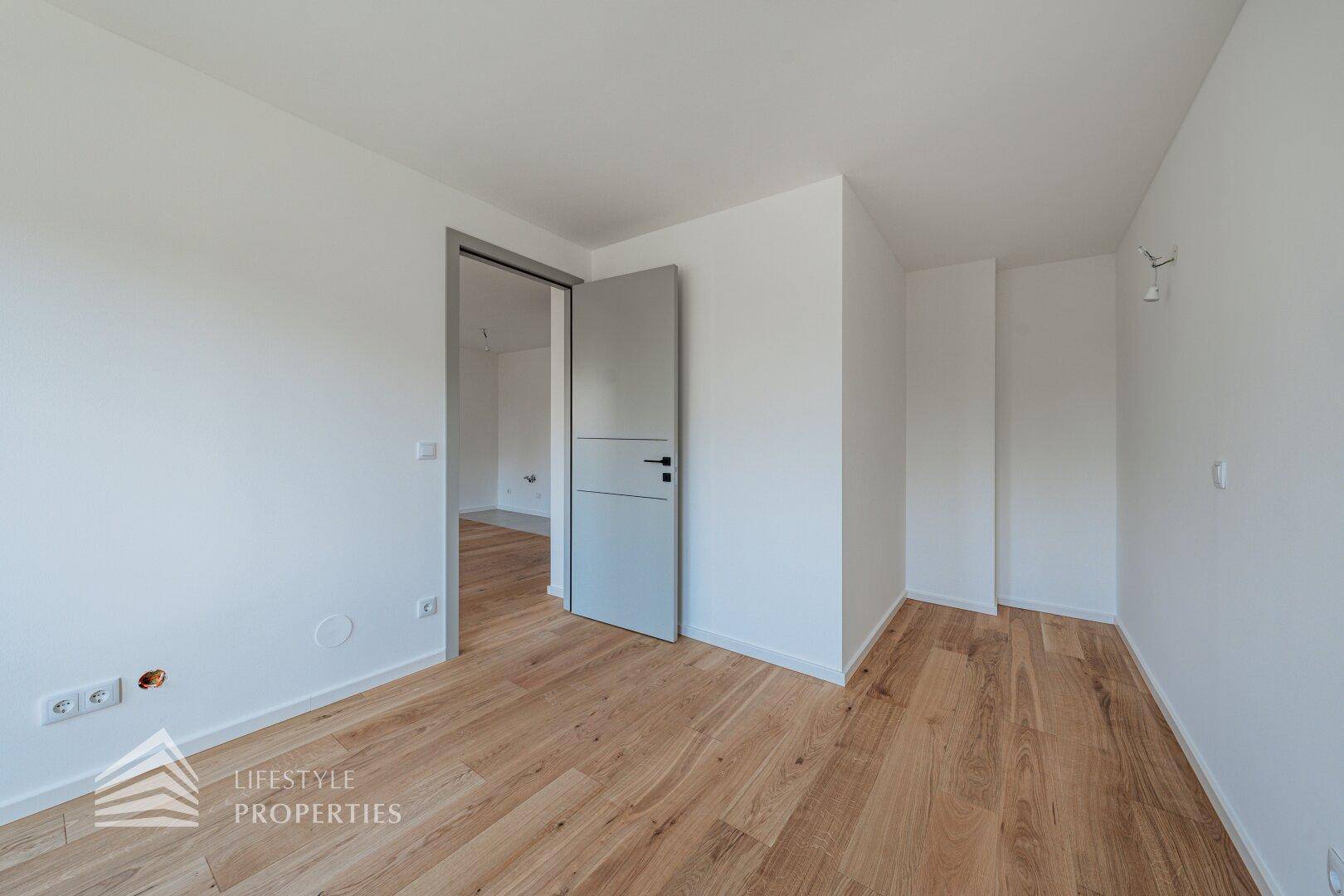 Helles Schlafzimmer mit neuem Holzboden und Zugang zu einem weiteren Raum.