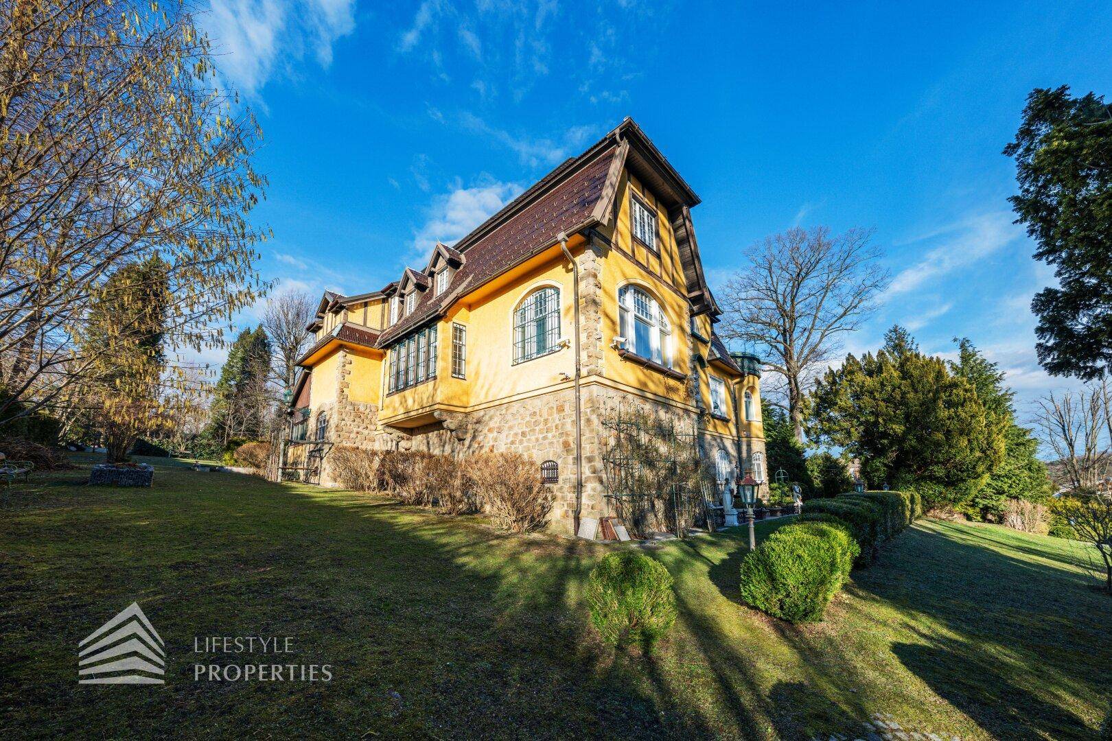Seitenansicht der historischen Villa mit markantem Mansarddach und terrassiertem Gartenbereich.