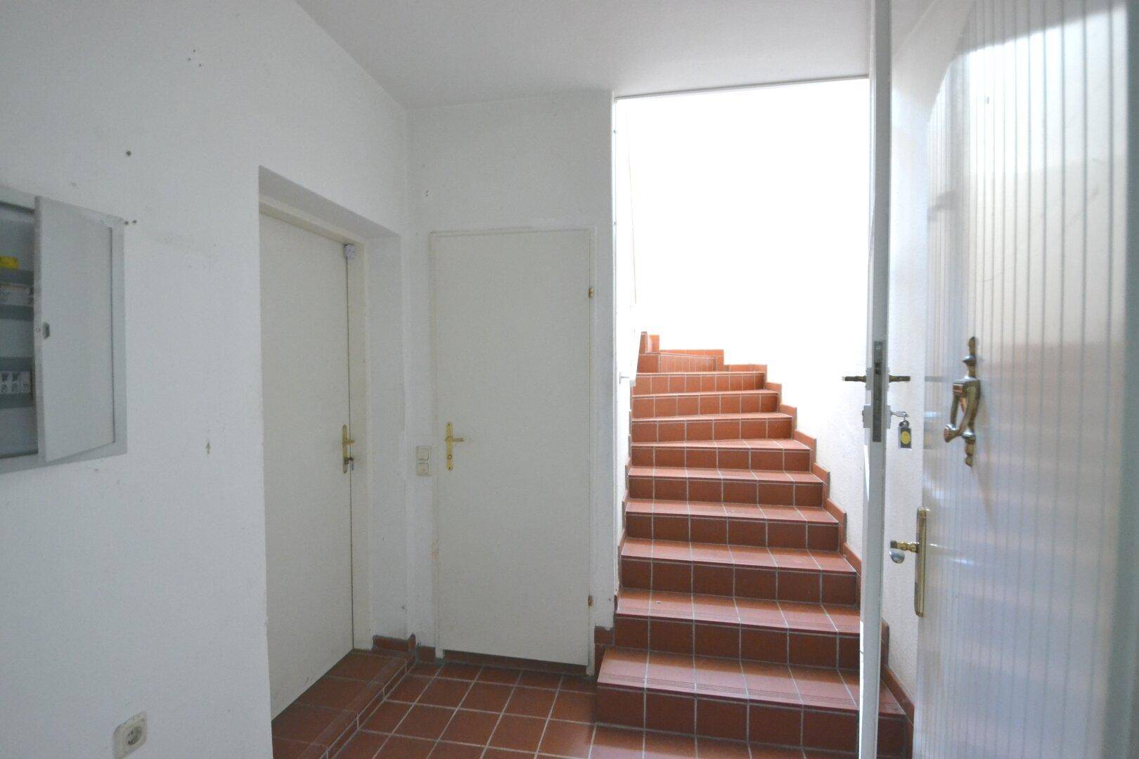 Eingangsbereich mit gefliestem Boden und einer Treppe, die in die oberen Stockwerke führt.