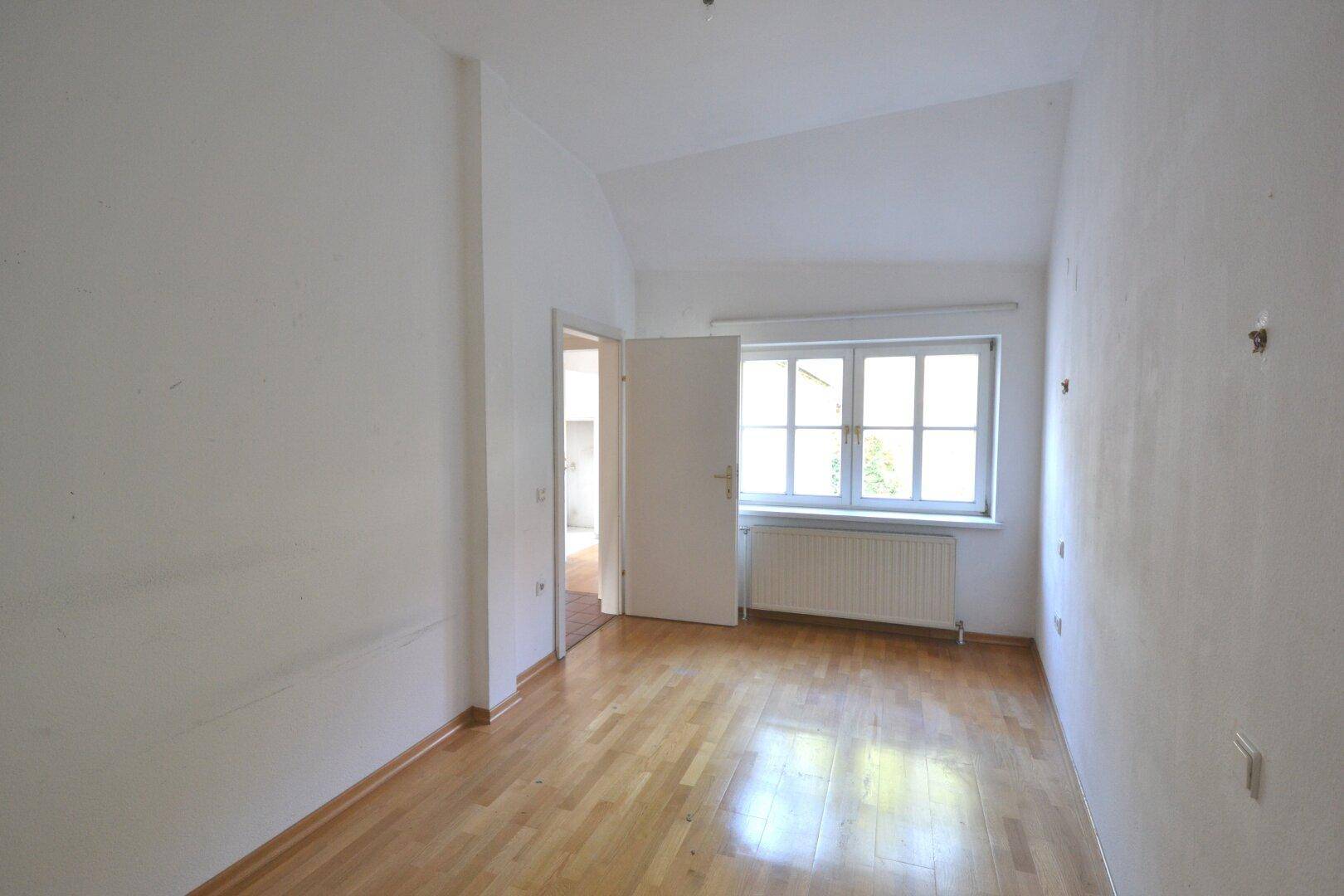 Leerer Raum mit Holzboden, einem Fenster und weiß gestrichenen Wänden.