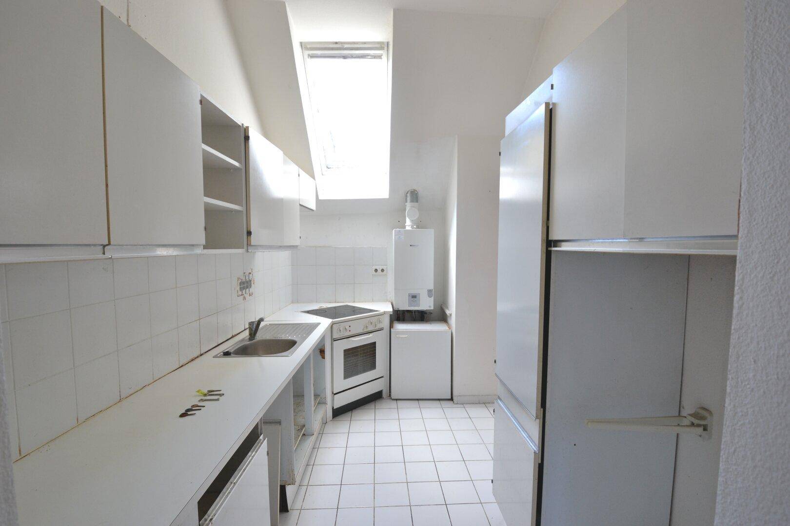 Kleine, einfache Küche mit weißen Fliesen, Dachfenster und älteren Einbaugeräten.