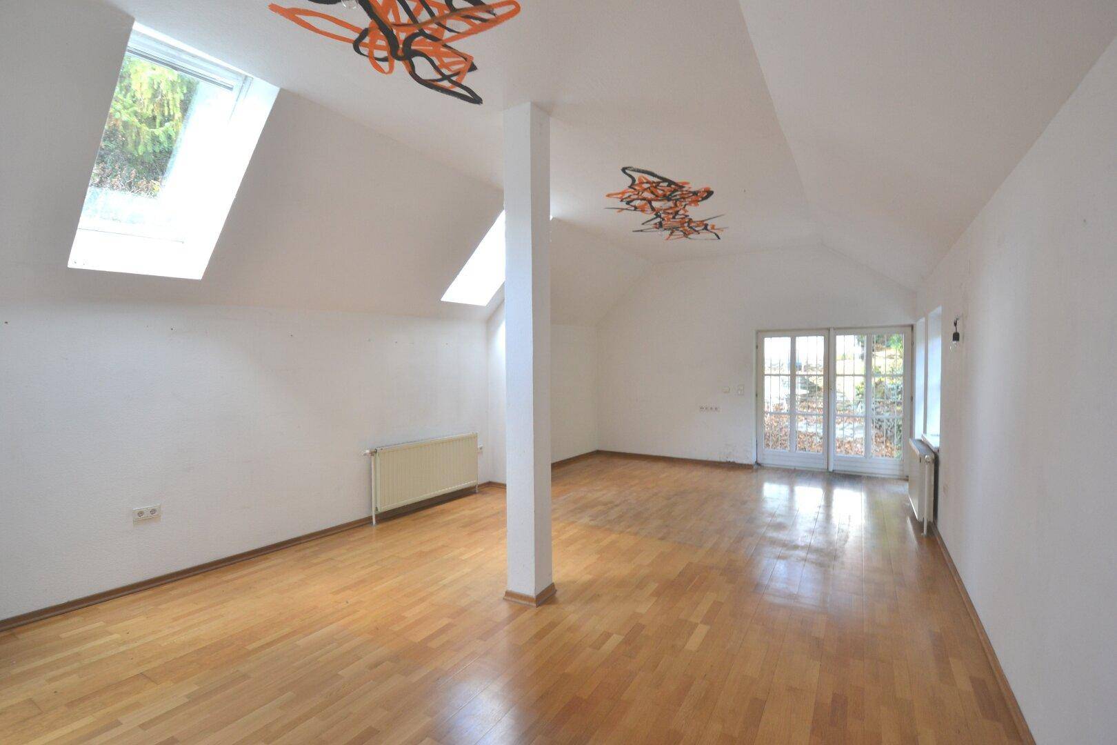 Leeres Wohnzimmer mit Holzboden, Dachschrägen und zwei Dachfenstern für natürliches Licht.