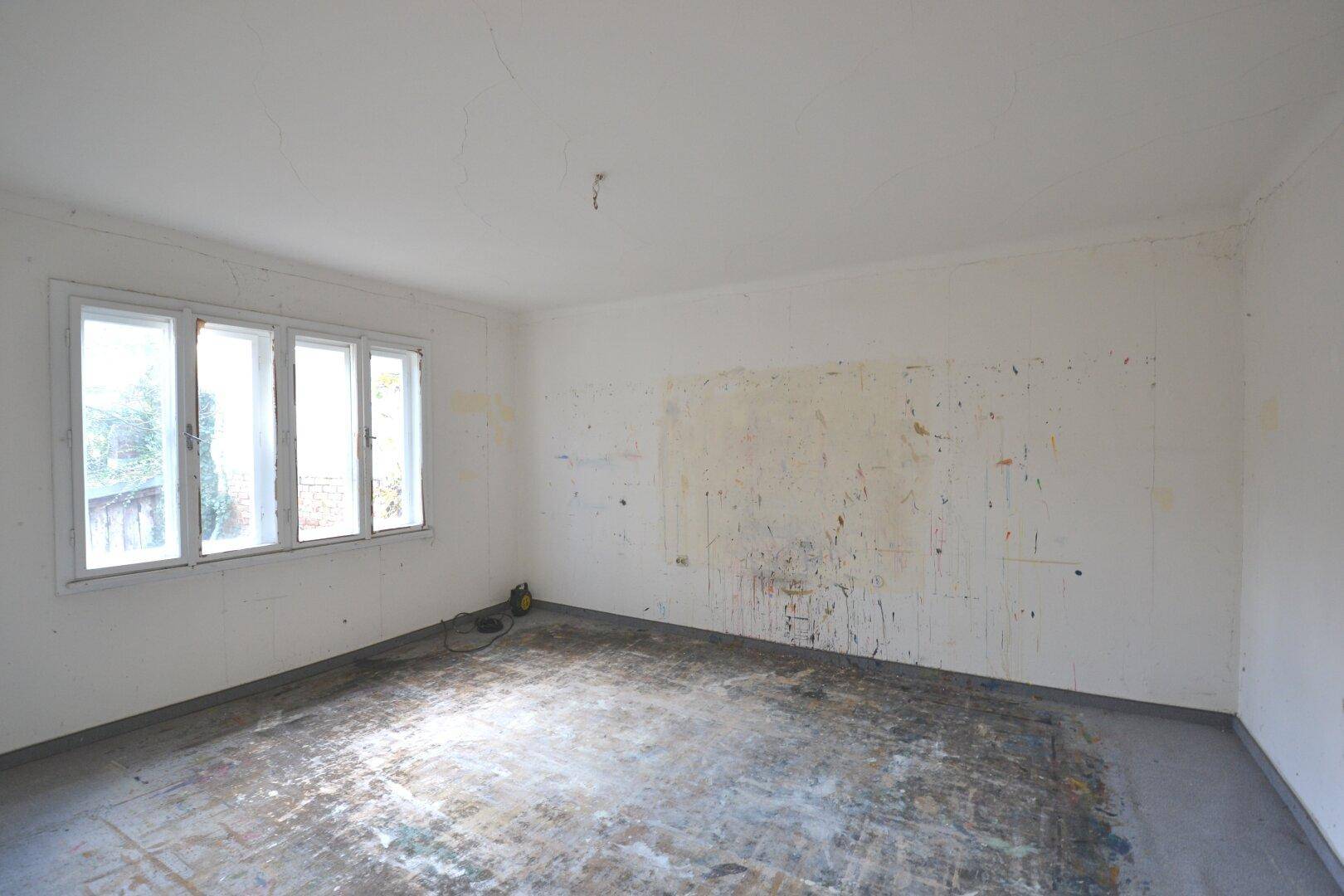 Leerer Raum mit großen Fenstern und Wänden, die auf eine umfassende Renovierung warten.