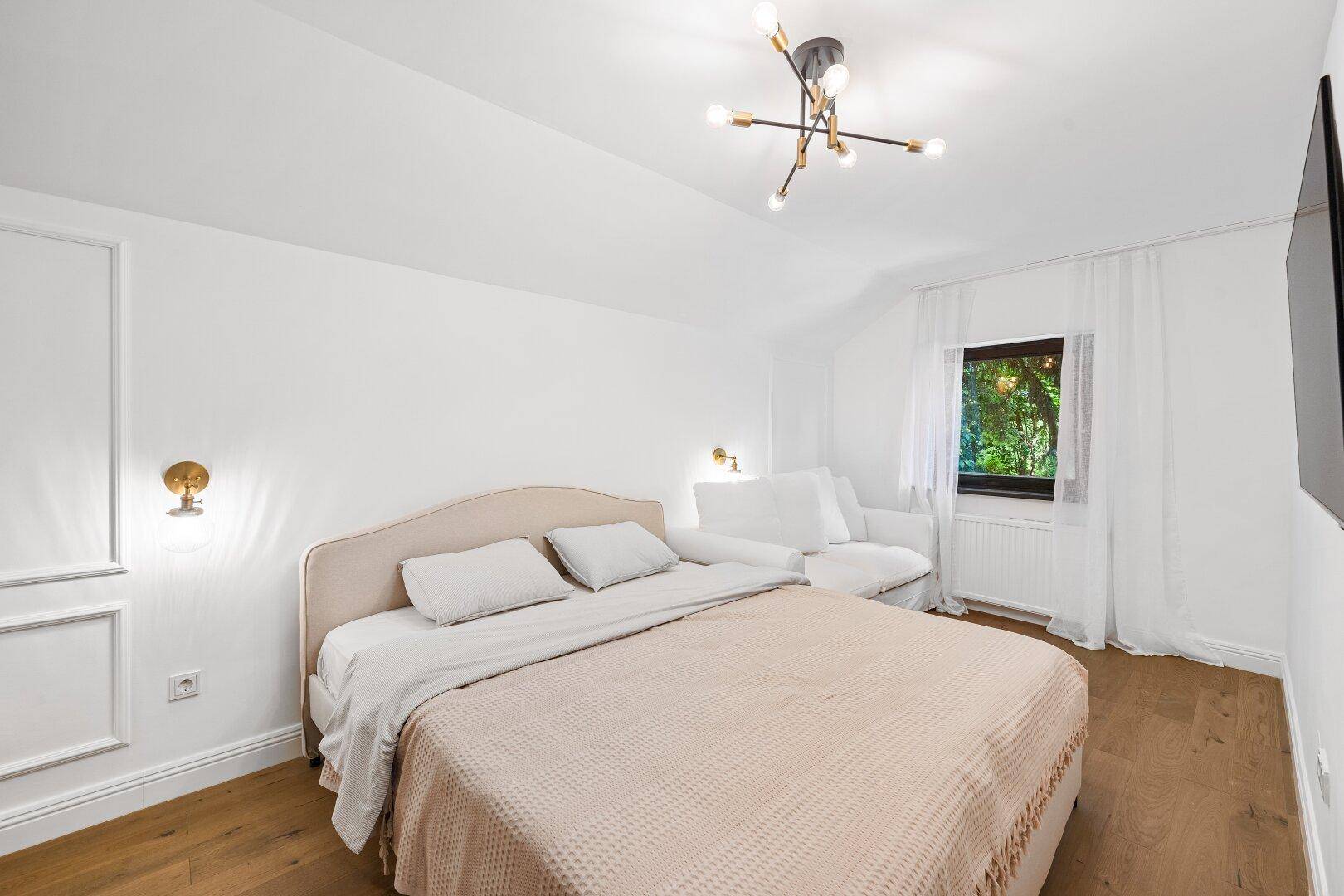 Gemütliches Schlafzimmer mit Doppelbett, Holzboden und Fenster mit Blick ins Grüne.