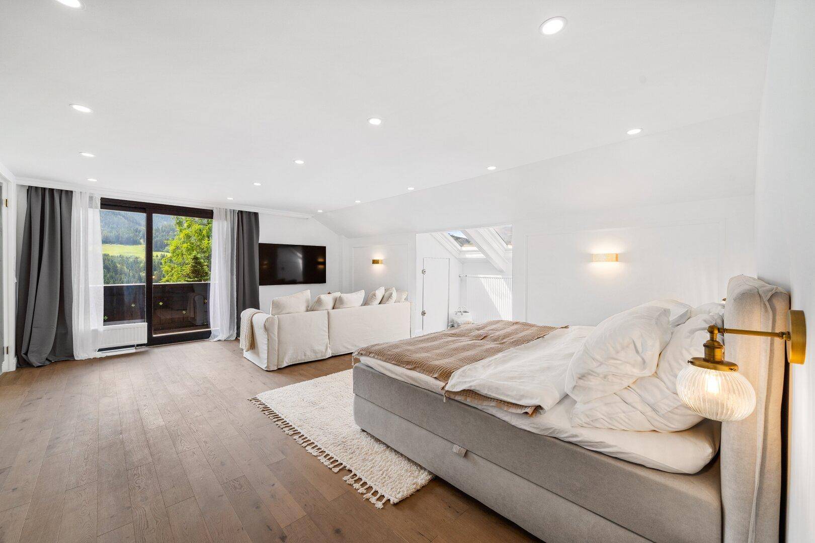 Geräumiges Schlafzimmer mit großem Bett, Holzboden und Blick auf die umliegende Natur.