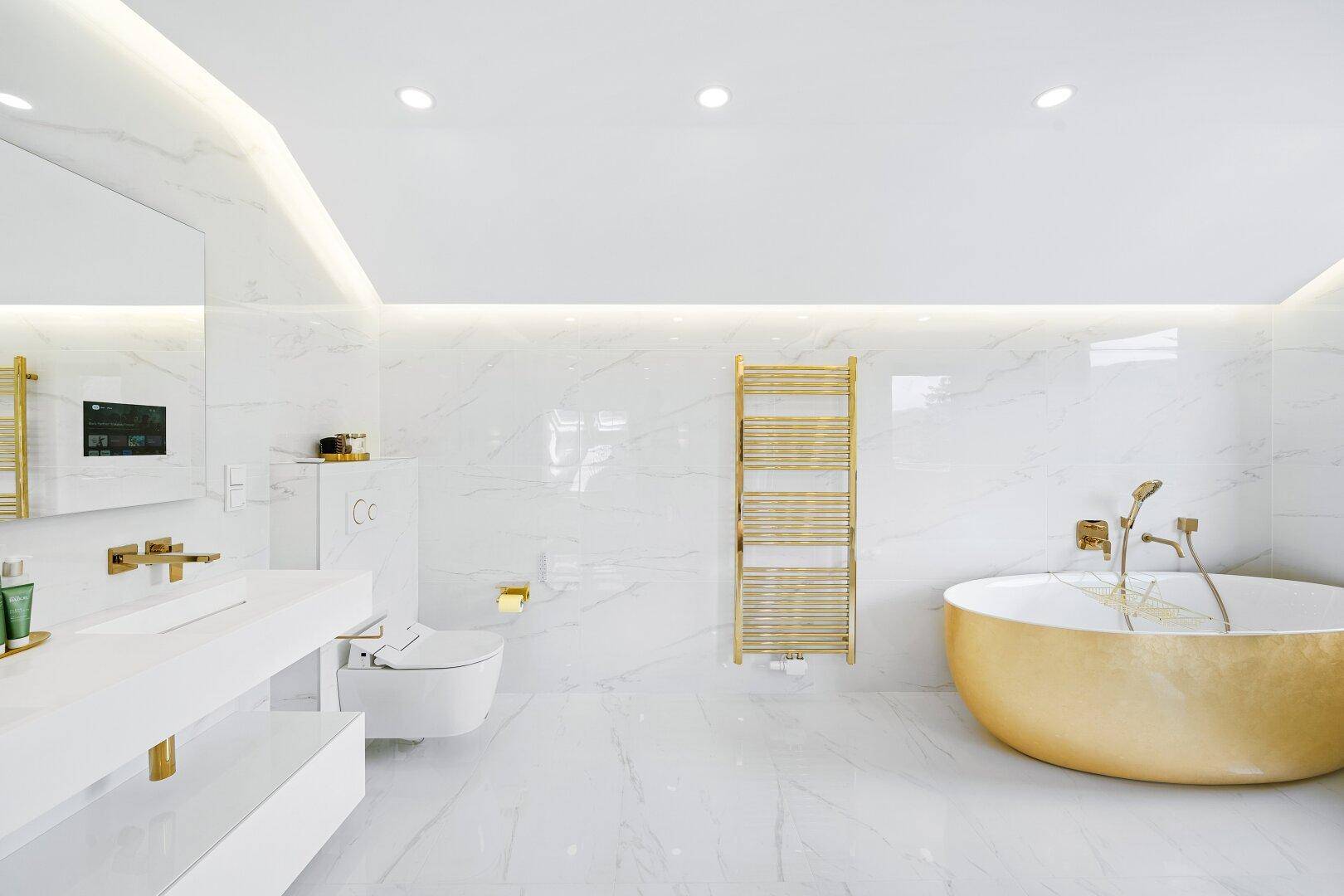 Elegantes Badezimmer mit weißen Marmorfliesen, goldener Badewanne und modernen Armaturen.