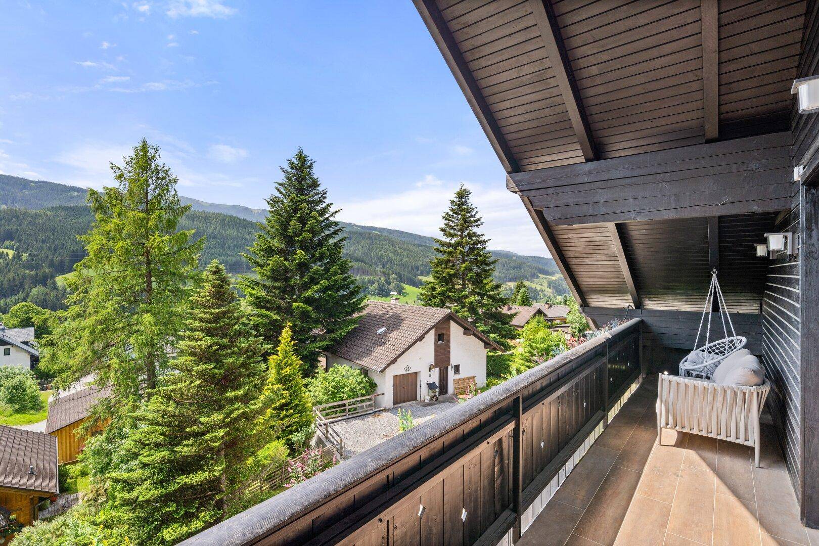 Großer Holzbalkon mit Hängesessel und weitem Blick auf die malerische Berglandschaft.