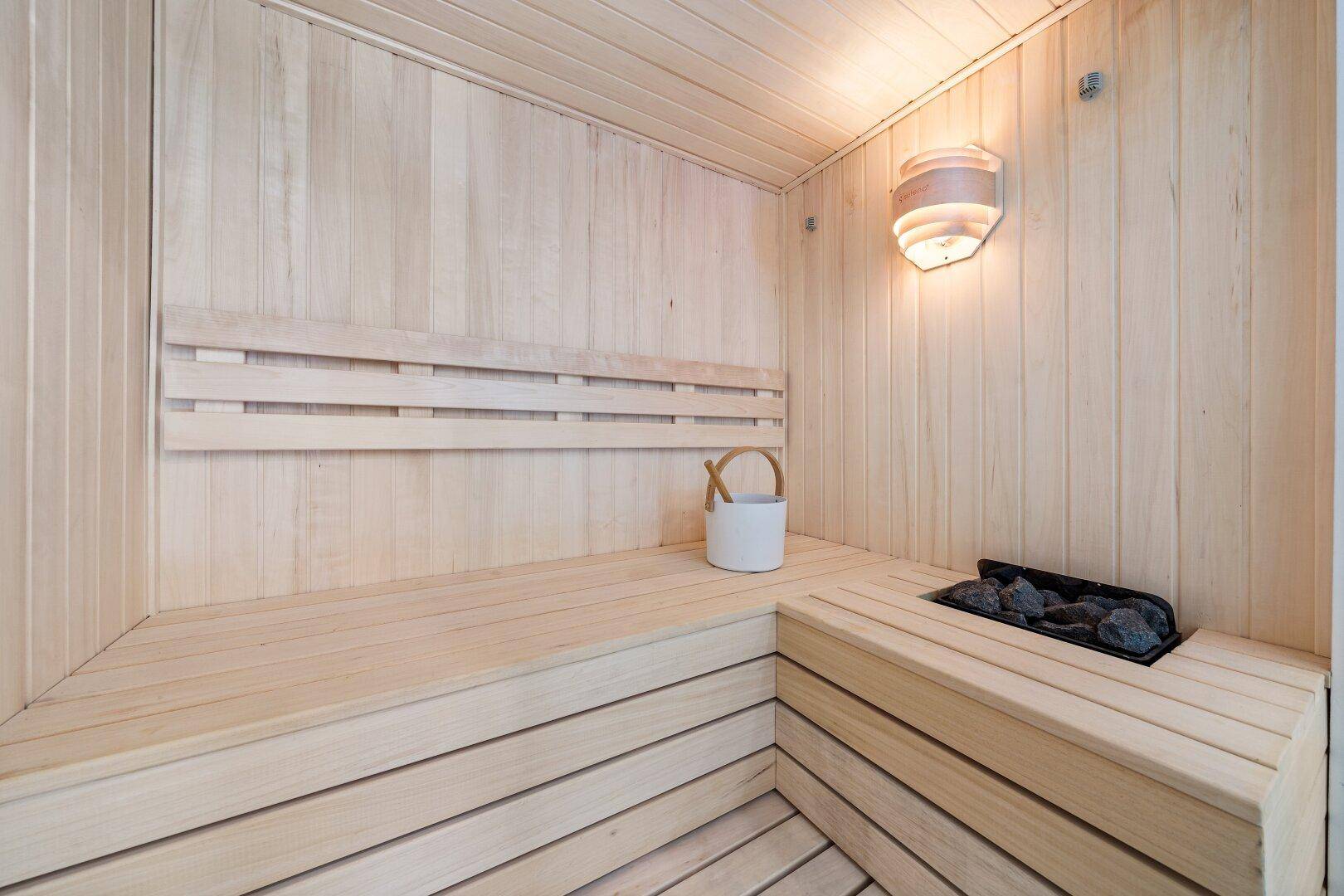 Helle Holzsauna mit traditionellem Ofen und Sitzbänken für entspannende Momente.