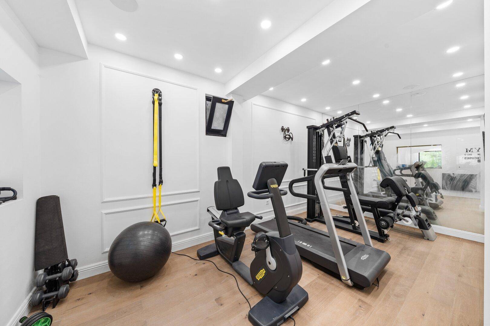 Privater Fitnessraum mit verschiedenen Trainingsgeräten, Spiegelwand und Holzfußboden.