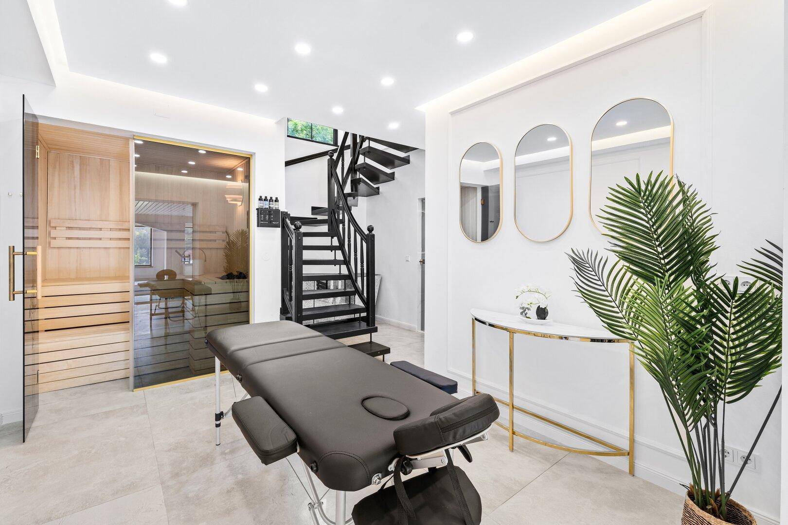 Entspannungsbereich mit Massageliege, Sauna und Zugang zu einer eleganten Treppe.