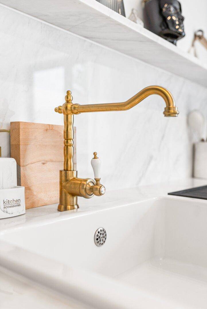 Detailaufnahme einer goldenen Armatur über einem weißen Spülbecken in der Küche.