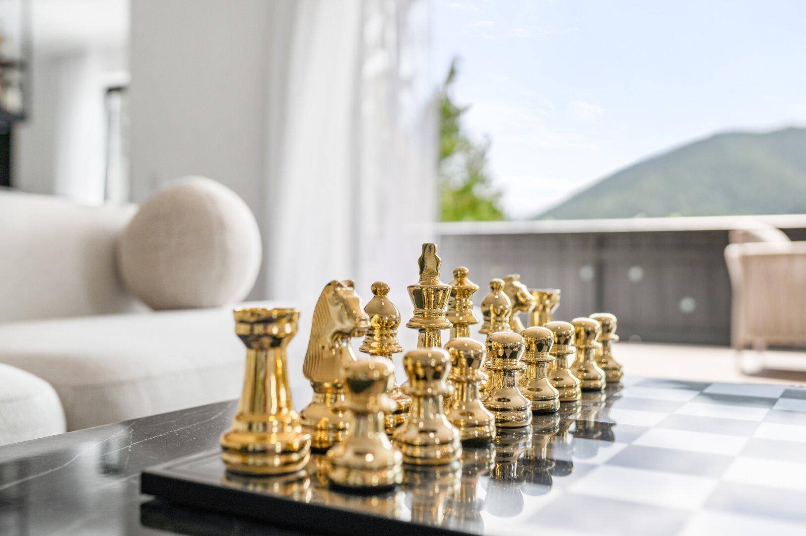 Schachbrett mit goldenen Figuren auf einem Tisch im hellen Wohnbereich mit Bergblick.