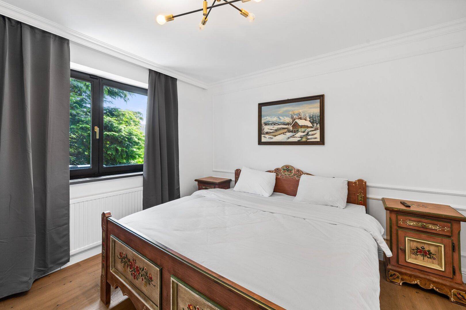 Schlafzimmer mit traditionellem Holzbett, Holzboden und Fenster mit Blick ins Grüne.