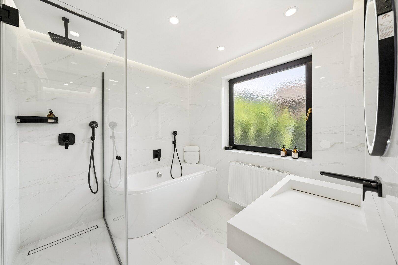 Modernes Badezimmer mit weißen Marmorfliesen, begehbarer Dusche, Badewanne und Fenster.