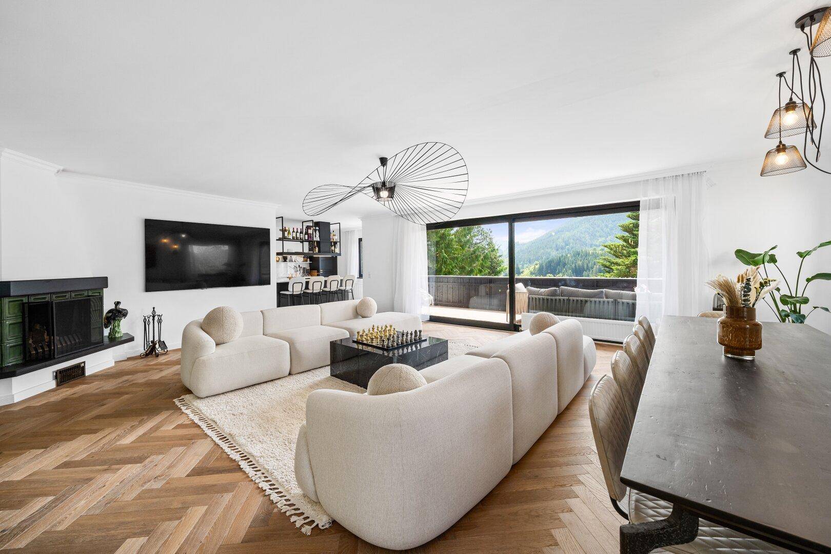 Geräumiger Wohnbereich mit Kamin, großem Fernseher und Zugang zu einem Balkon mit Bergblick.