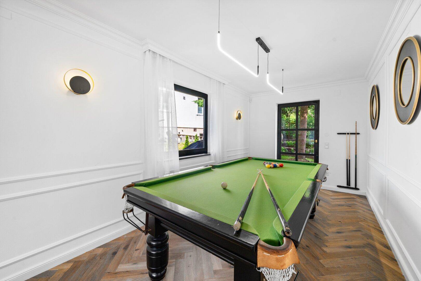 Spielzimmer mit Billardtisch, modernen Wandleuchten und Parkettboden.