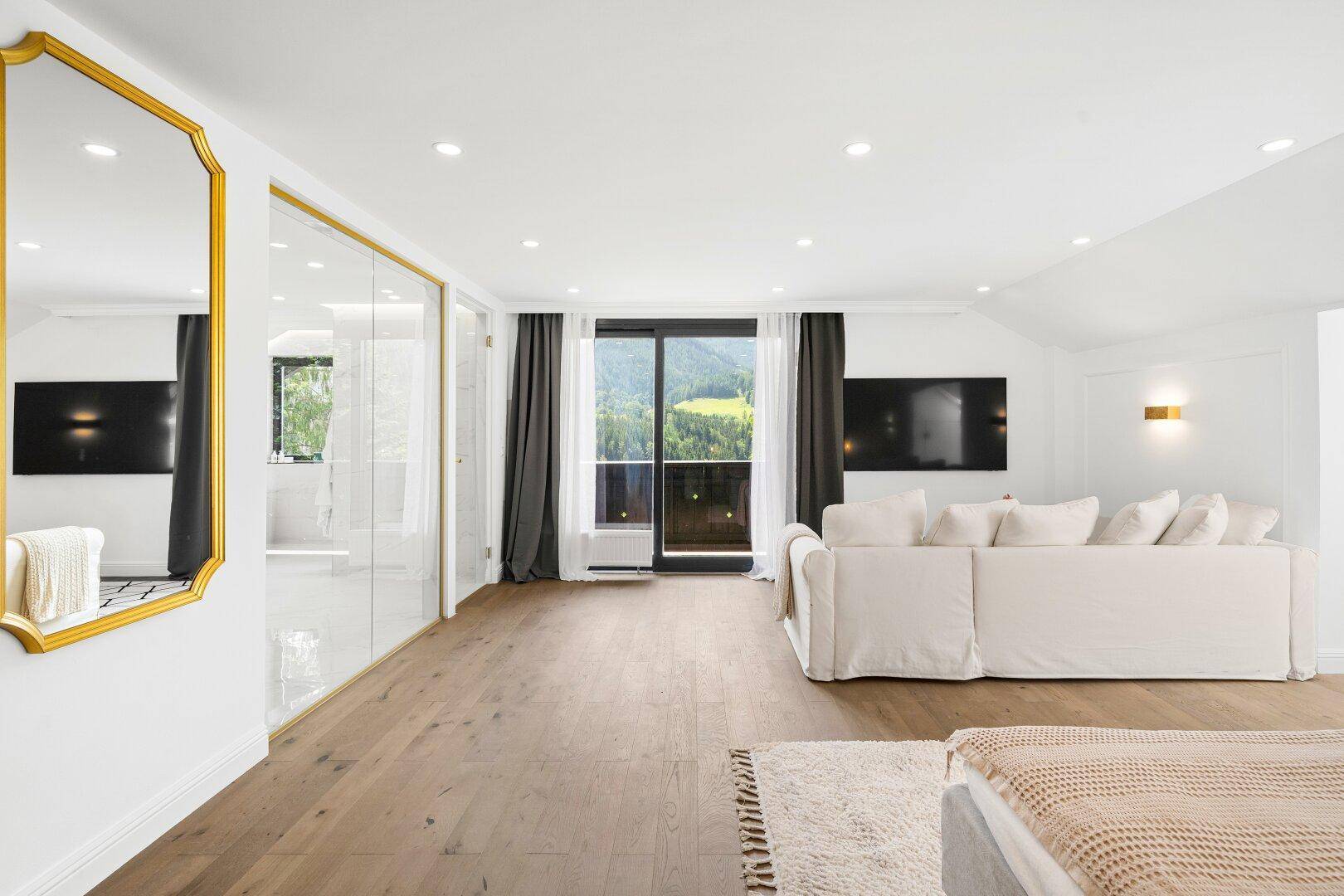 Helles Schlafzimmer mit Holzboden, Sofa und Zugang zu einem Balkon mit Bergblick.