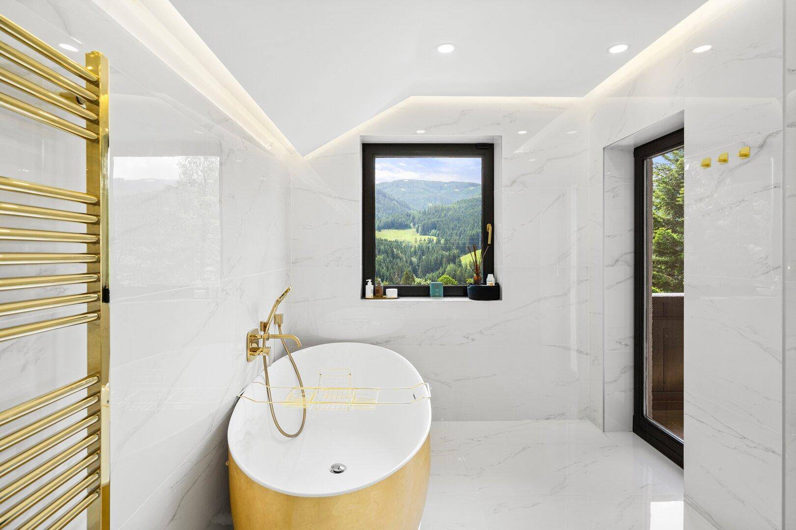 Helles Badezimmer mit freistehender Badewanne, Bergblick und goldfarbenem Handtuchhalter.