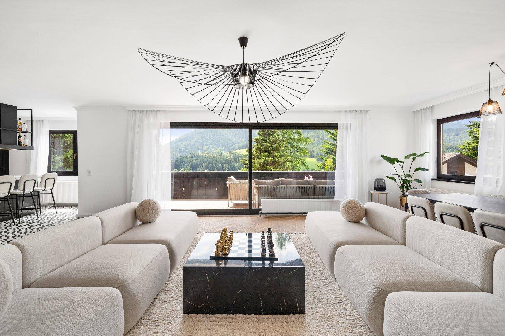 Helles Wohnzimmer mit modernem Design, bequemen Sofas und großem Fenster mit Bergblick.