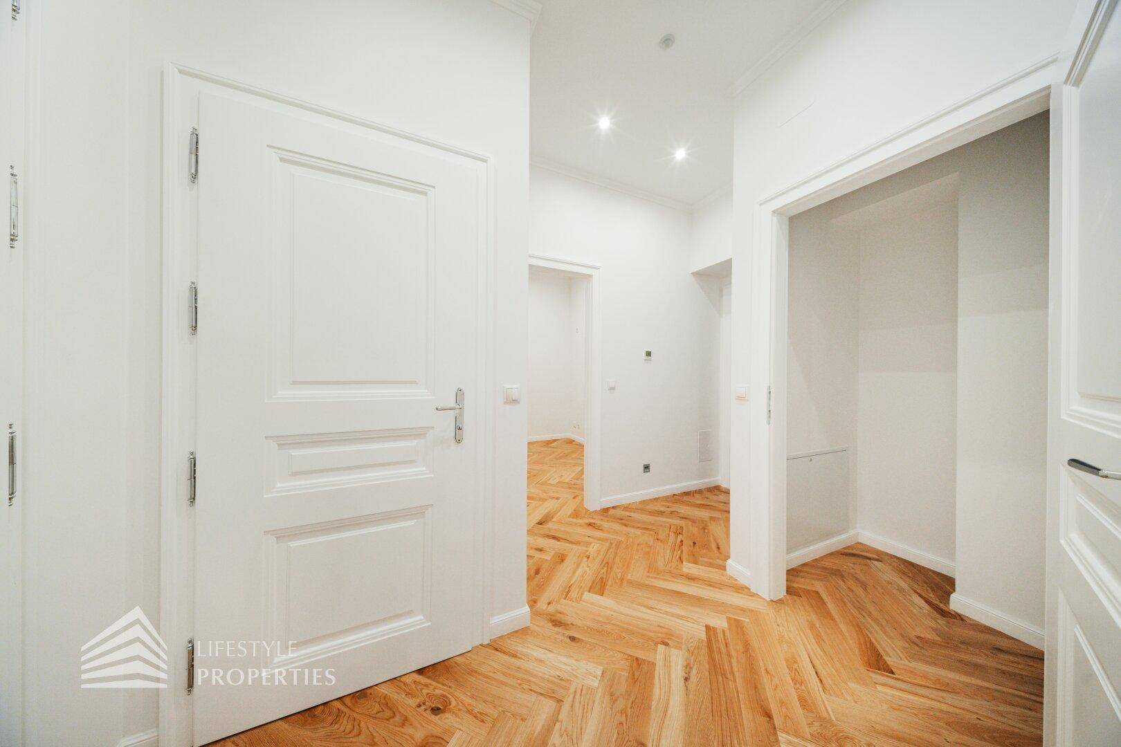 Heller Flur mit elegantem Fischgrätparkett, weißen Türen und moderner Deckenbeleuchtung.