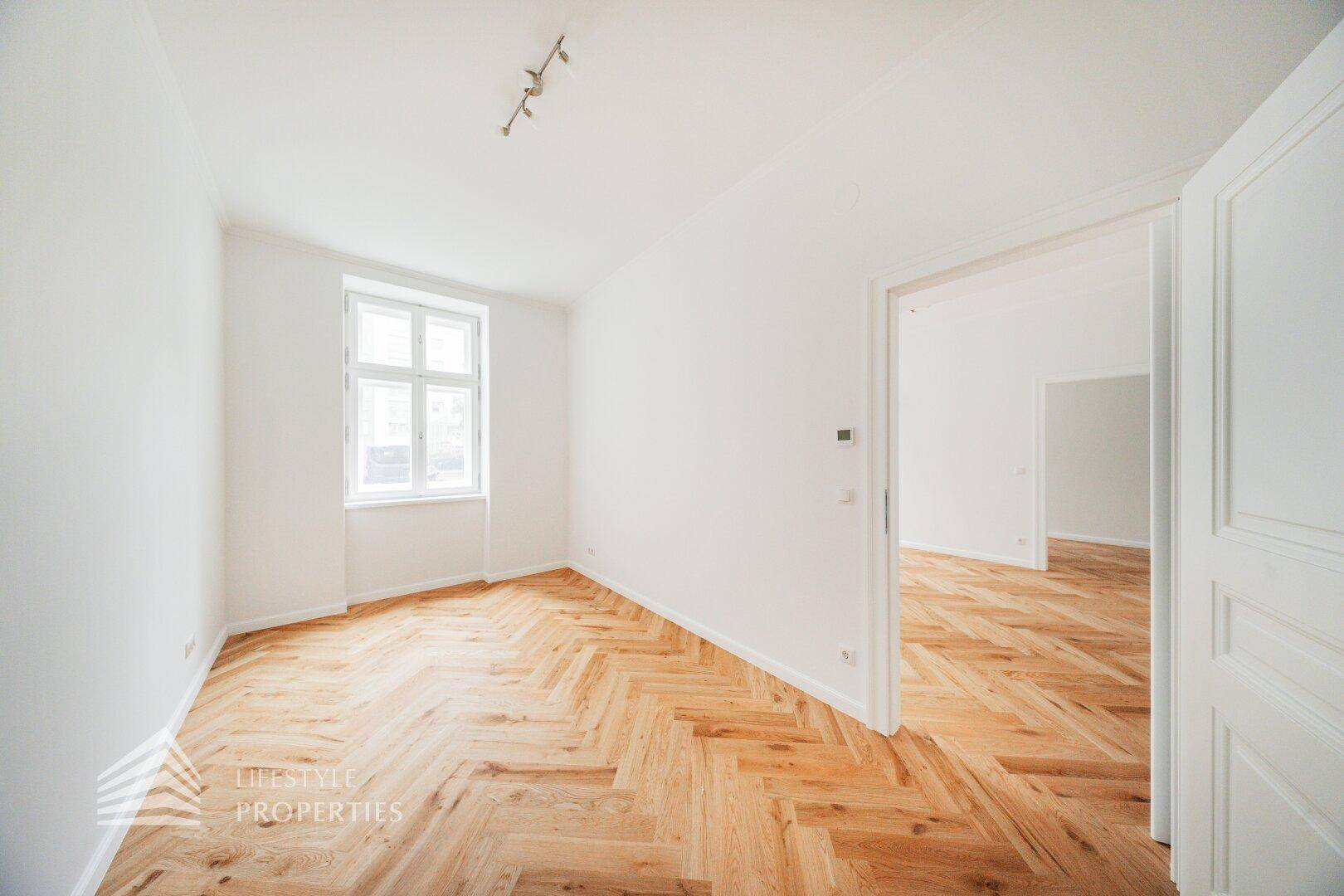 Heller Raum mit Fischgrätparkett und hohen Decken, ideal für Wohn- oder Schlafzimmer.