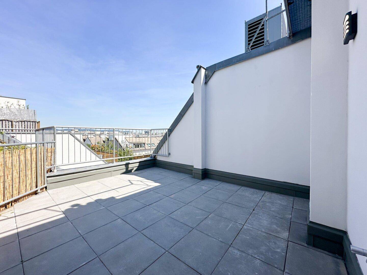 Geräumige Dachterrasse mit Fliesenboden und Blick über die Stadt.