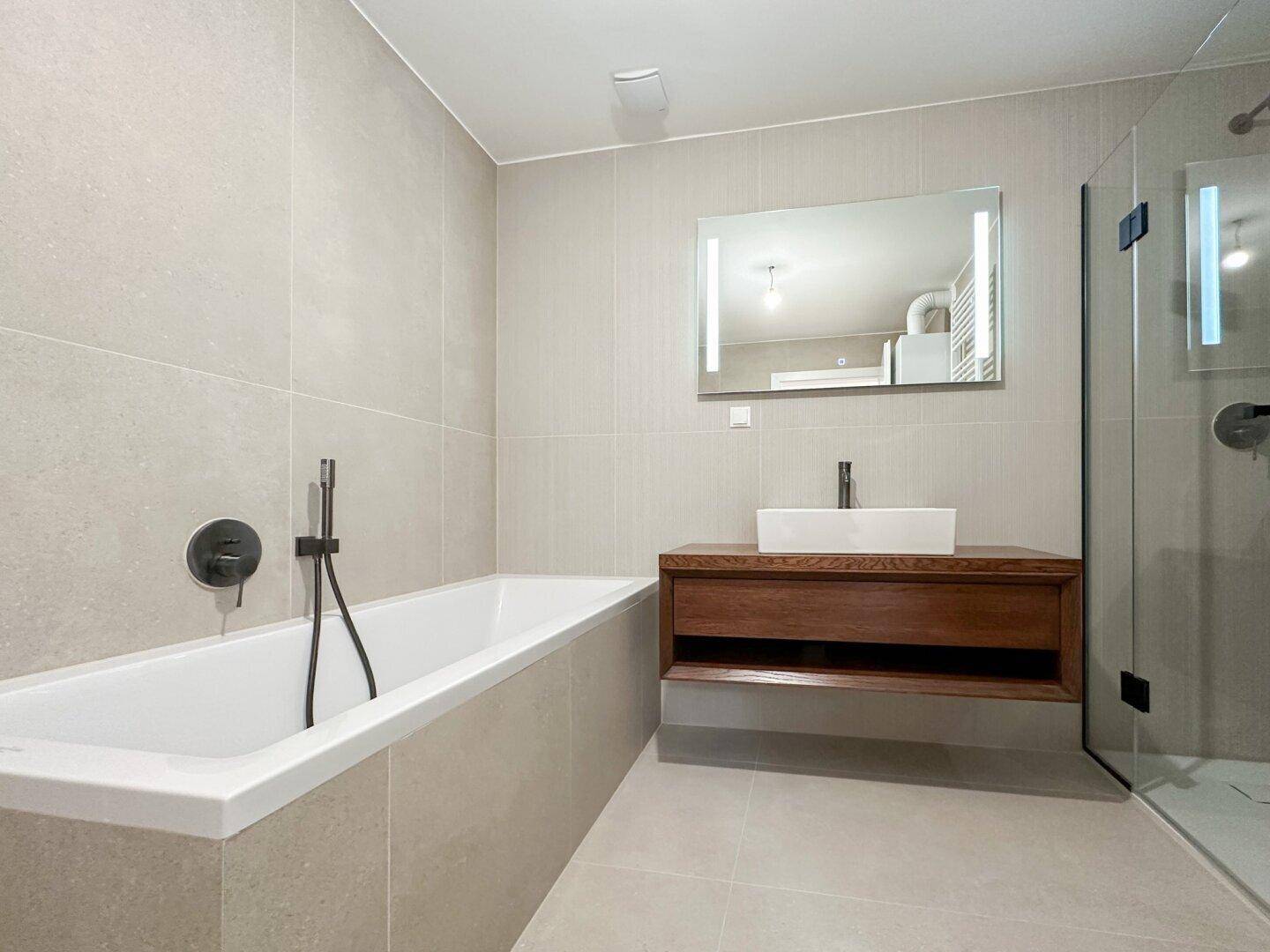 Elegantes Badezimmer mit Badewanne, Waschtisch und großer Duschkabine.