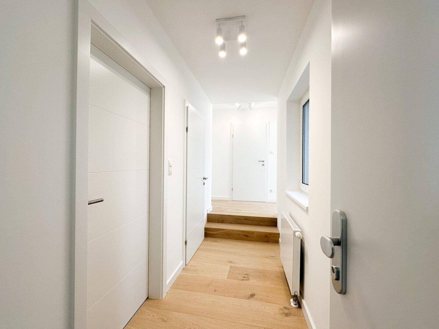 Heller Flur mit Holzparkettboden, weißen Türen und moderner Beleuchtung.