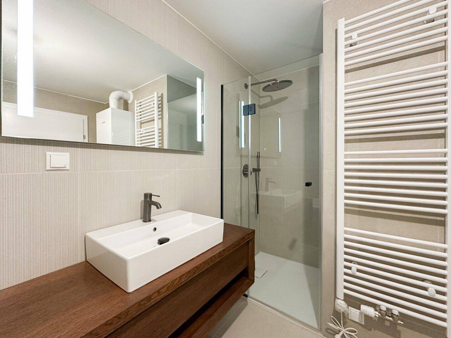 Modernes Badezimmer mit Waschtisch, großer Dusche und beheiztem Handtuchhalter.