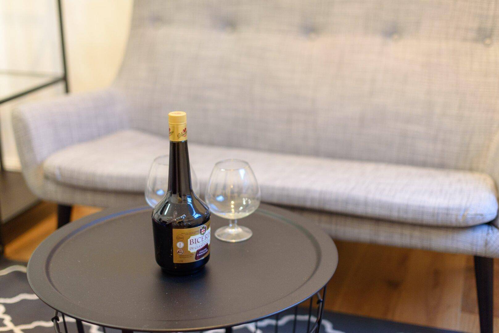 Nahaufnahme eines Couchtisches mit Getränk und Gläsern vor einem modernen grauen Sofa.