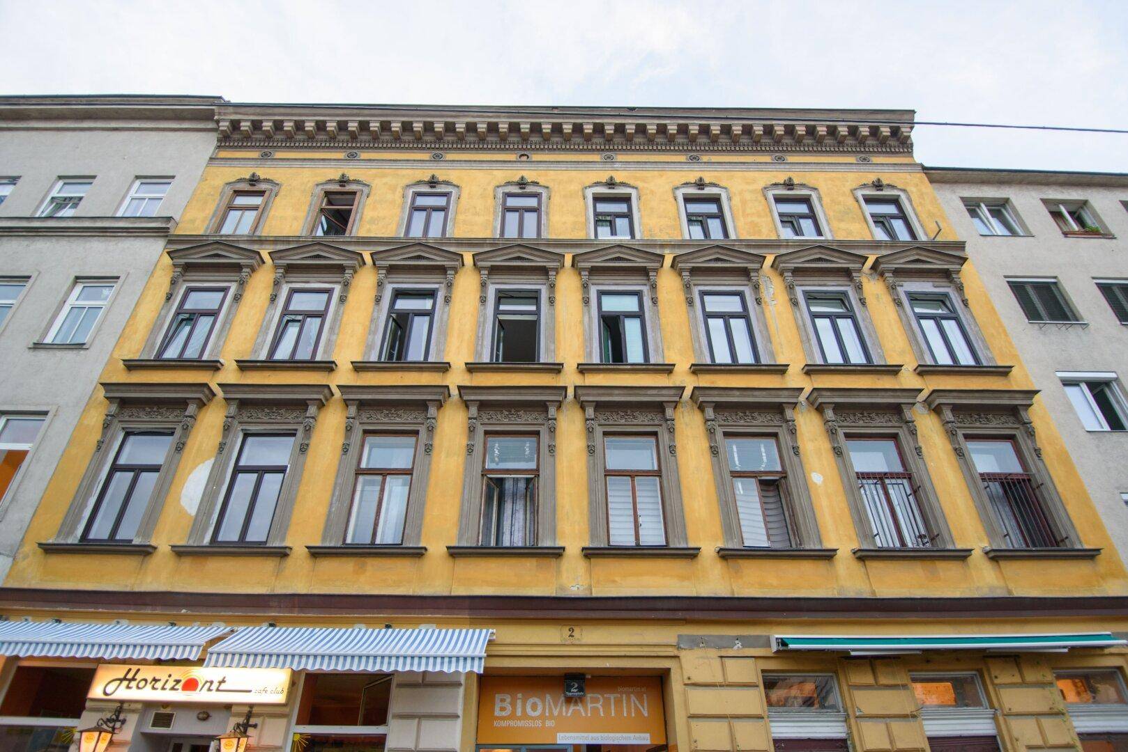 Historische Fassade eines mehrstöckigen Gebäudes mit zahlreichen Fenstern und gelbem Anstrich.