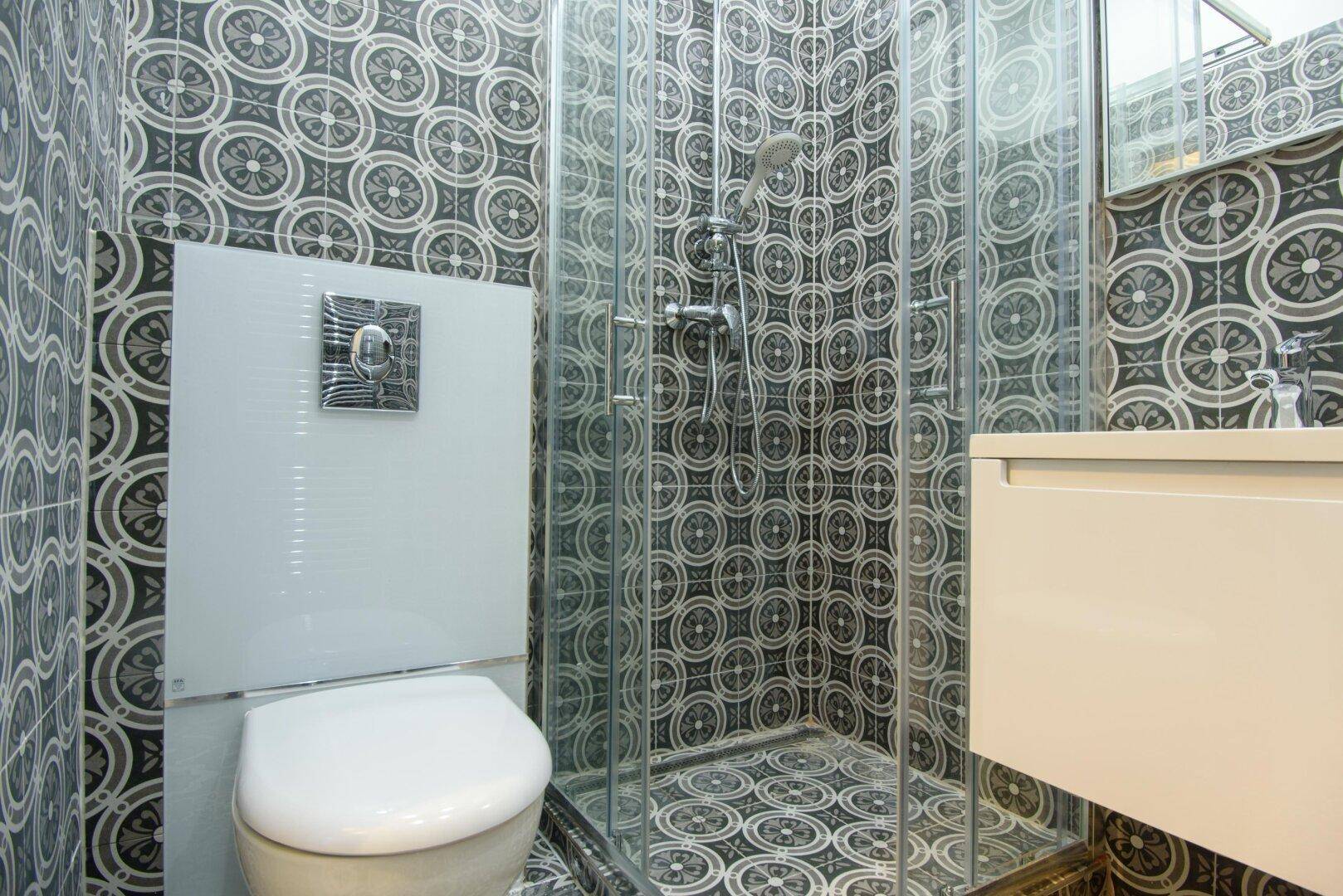 Badezimmer mit Duschkabine und wandhängendem WC, komplett gefliest in modernem Muster.