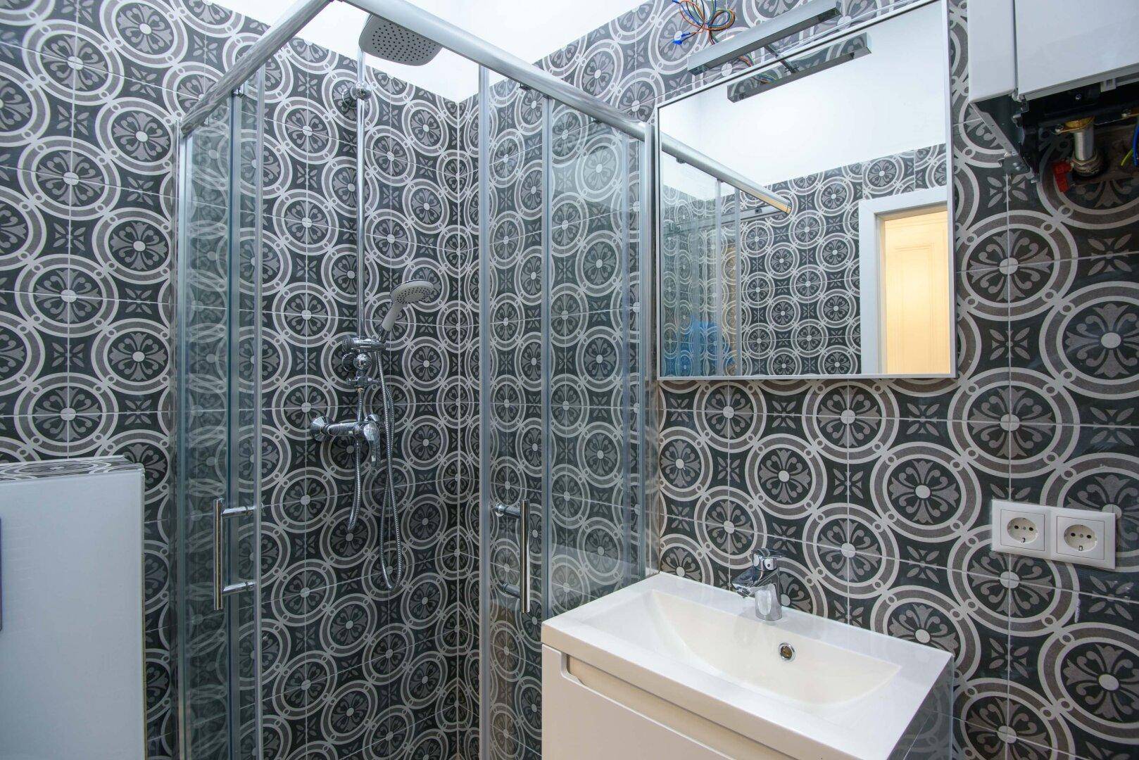 Modernes Badezimmer mit Duschkabine, Waschbecken und auffälligen gemusterten Fliesen.