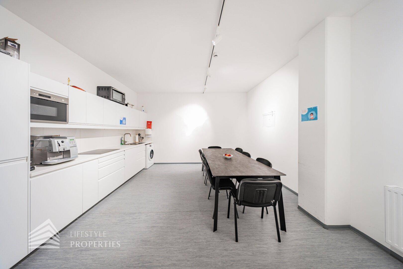 Helle und funktionale Büroküche mit weißen Einbauschränken und einem Esstisch.