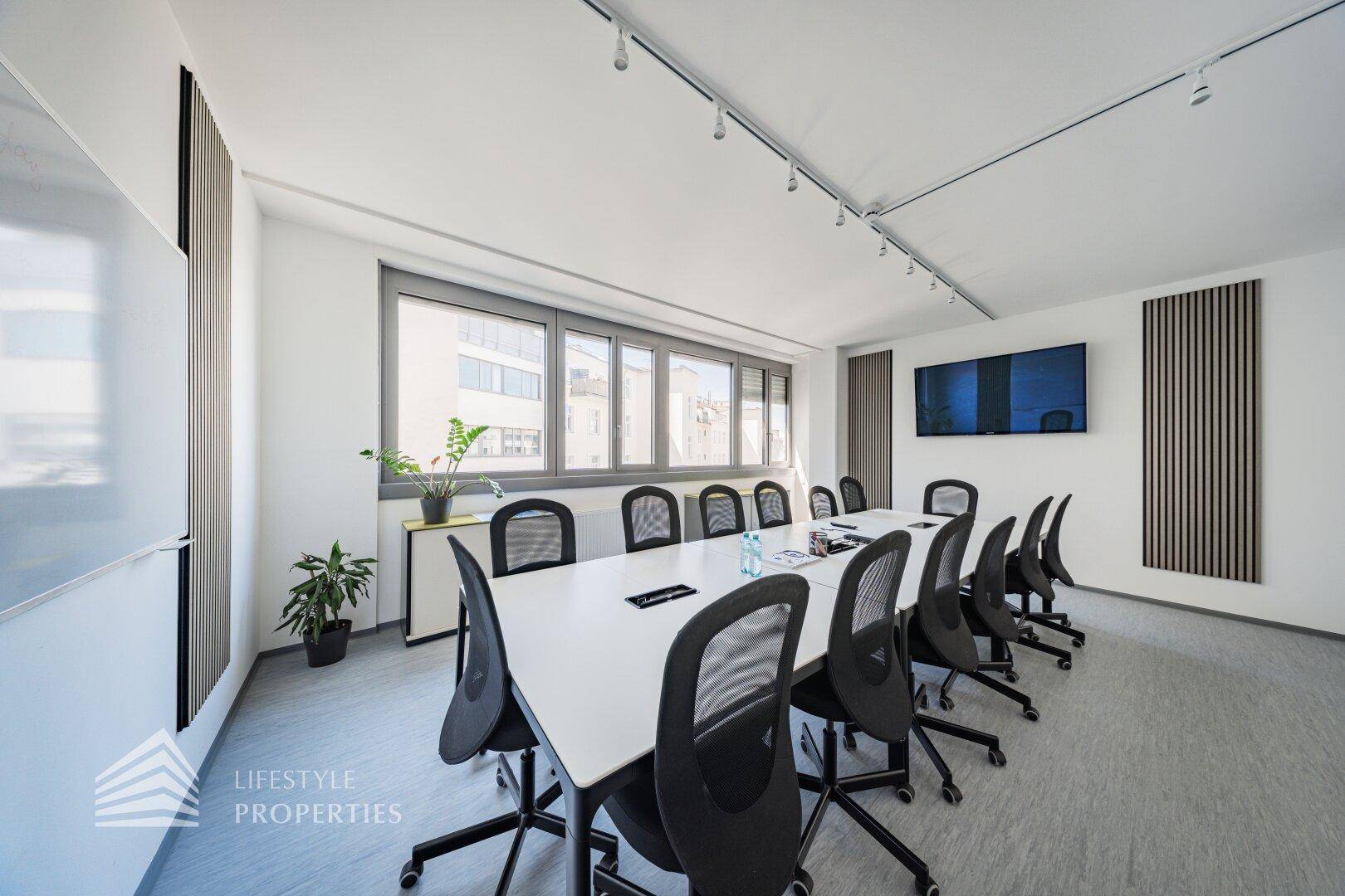 Helles Besprechungszimmer mit großem Konferenztisch, vielen Stühlen und Pflanzen als Dekoration.