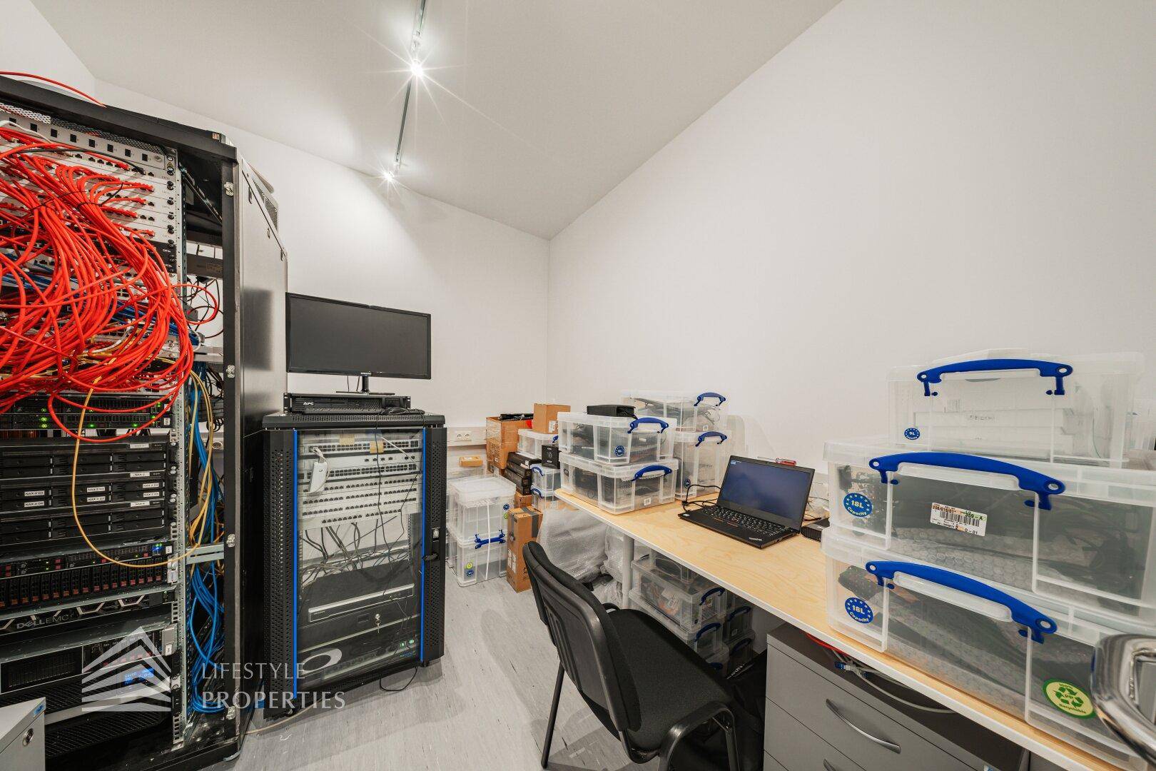 Serverraum mit mehreren Racks, Verkabelung und einem Arbeitsplatz für technische Aufgaben.
