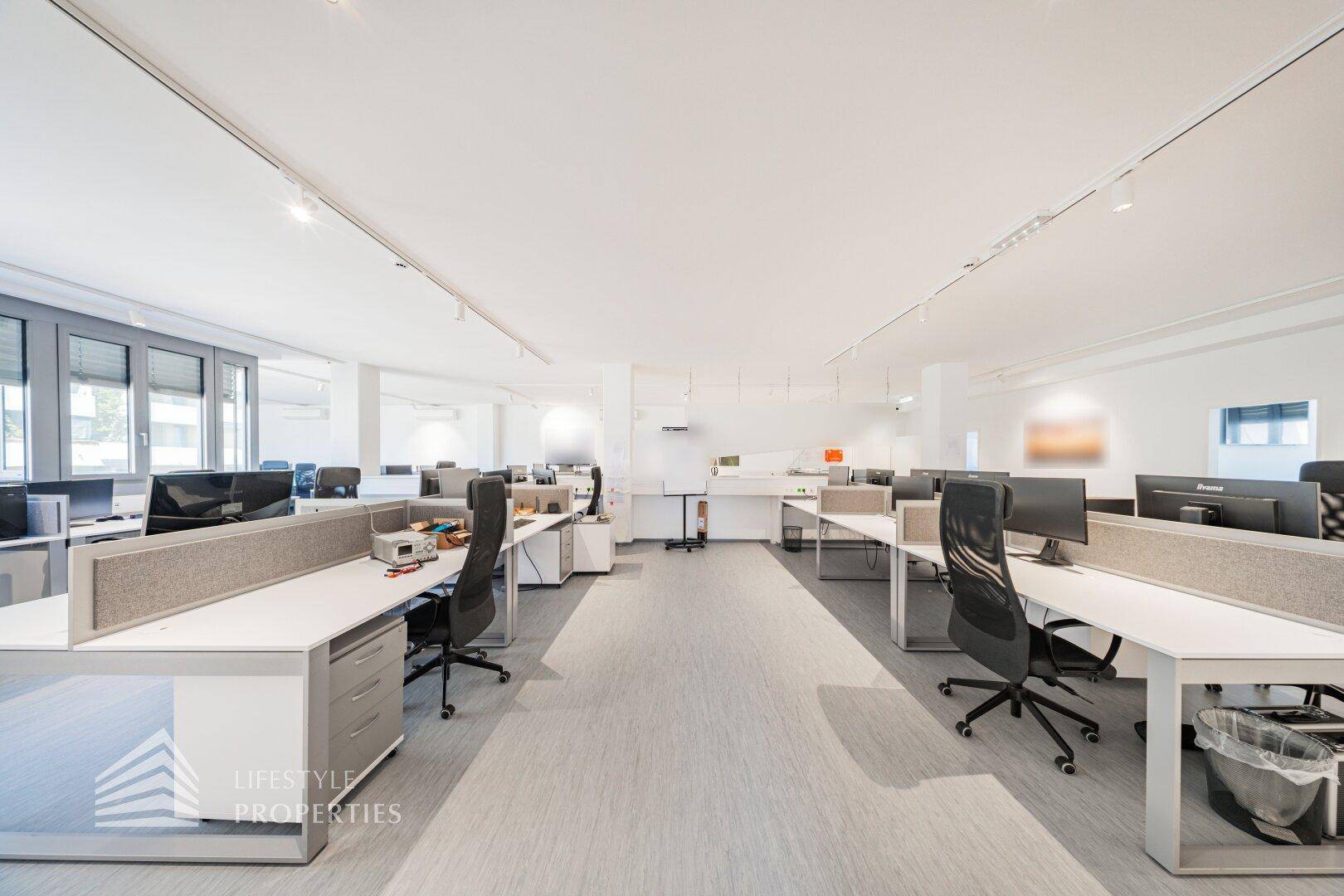 Offenes Büro mit Reihen von Schreibtischen, ergonomischen Stühlen und guter Beleuchtung.