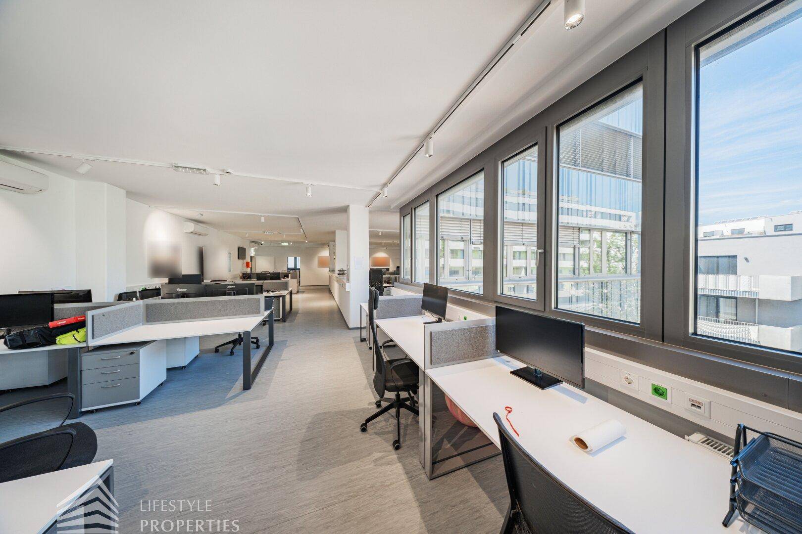 Helles Büro mit großen Fenstern, die viel Tageslicht hereinlassen und einen Blick nach draußen bieten.